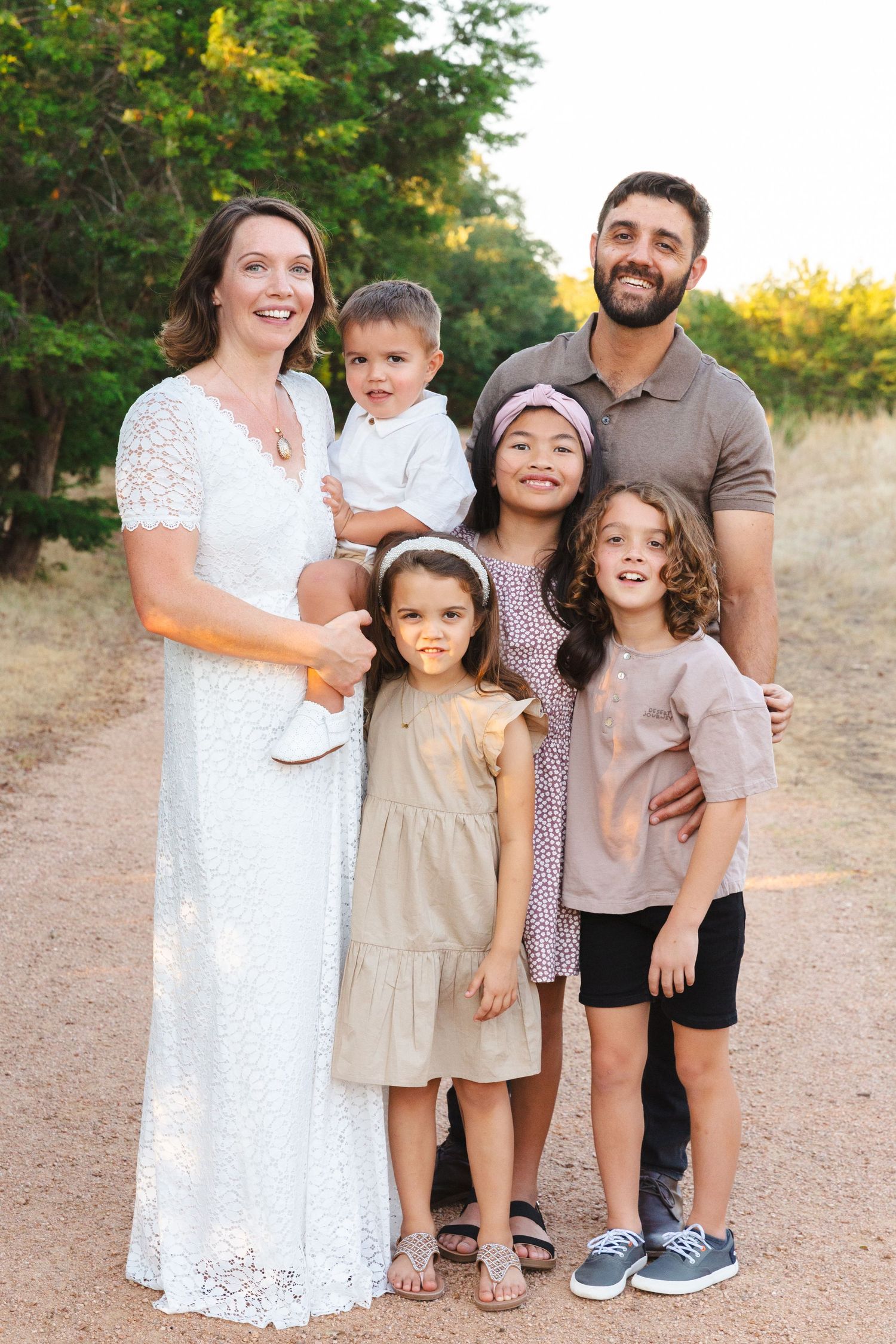 Family of six in coordinated outfits posing on dirt path during golden hour.