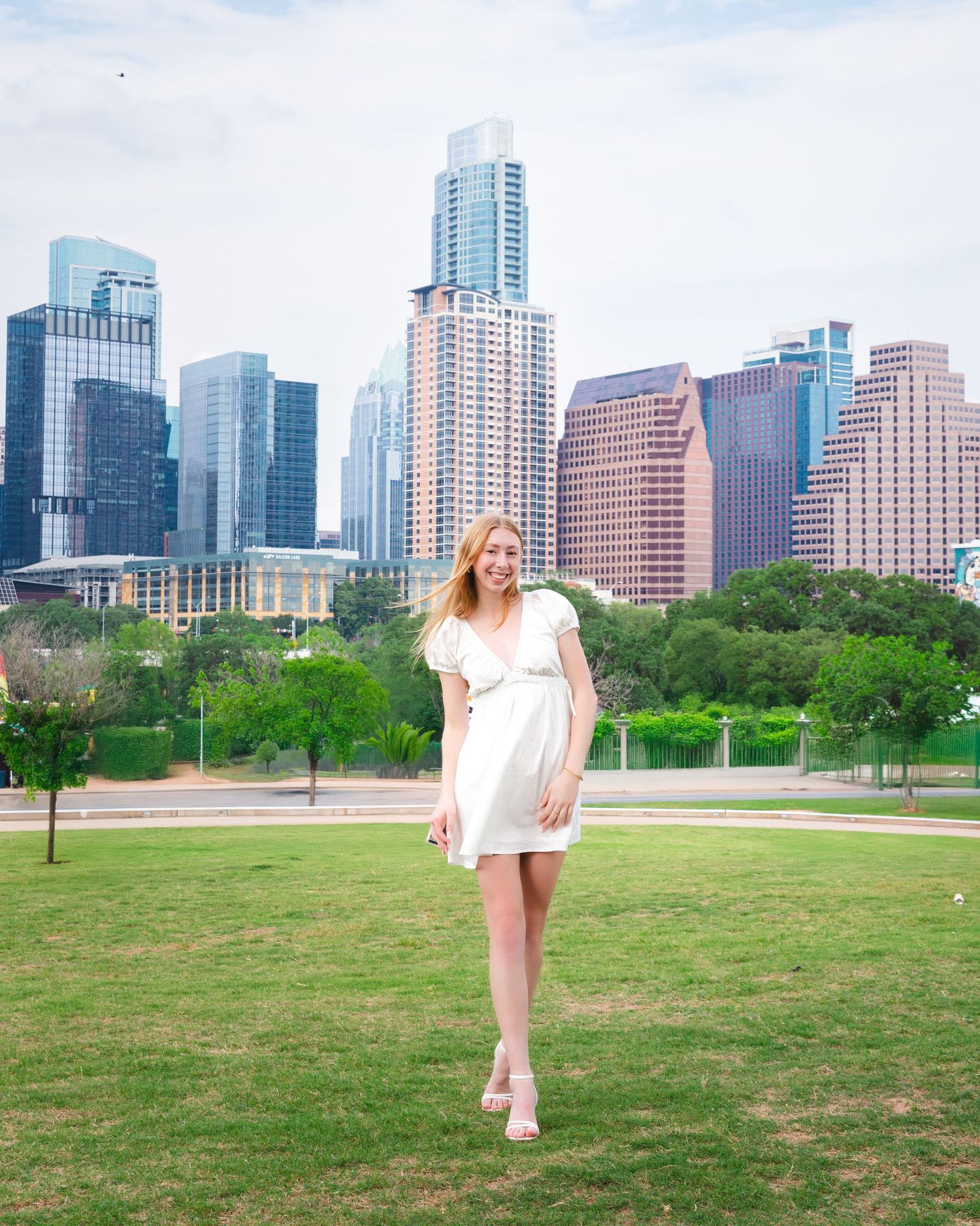 Senior session in Austin, TX. Person in white dress poses in front of Austin Texas city skyline.