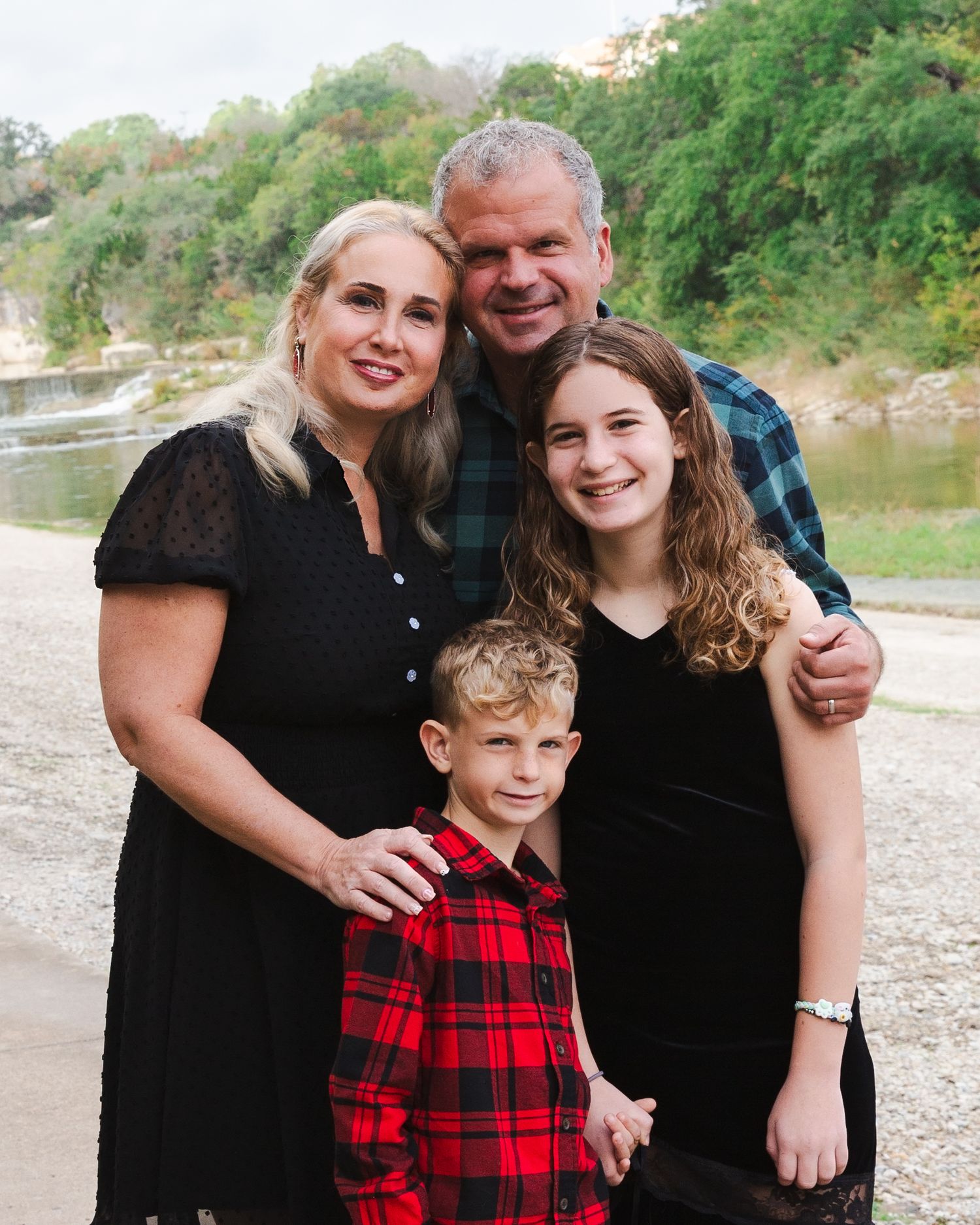 Family group in black and red plaid clothing posing together outdoors near a riverbank.