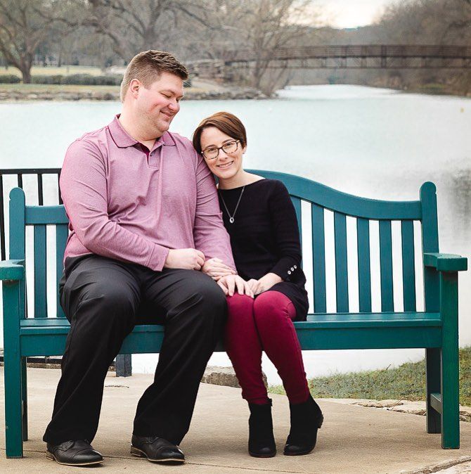 A couple shares a tender moment while sitting on a teal park bench near a lake.