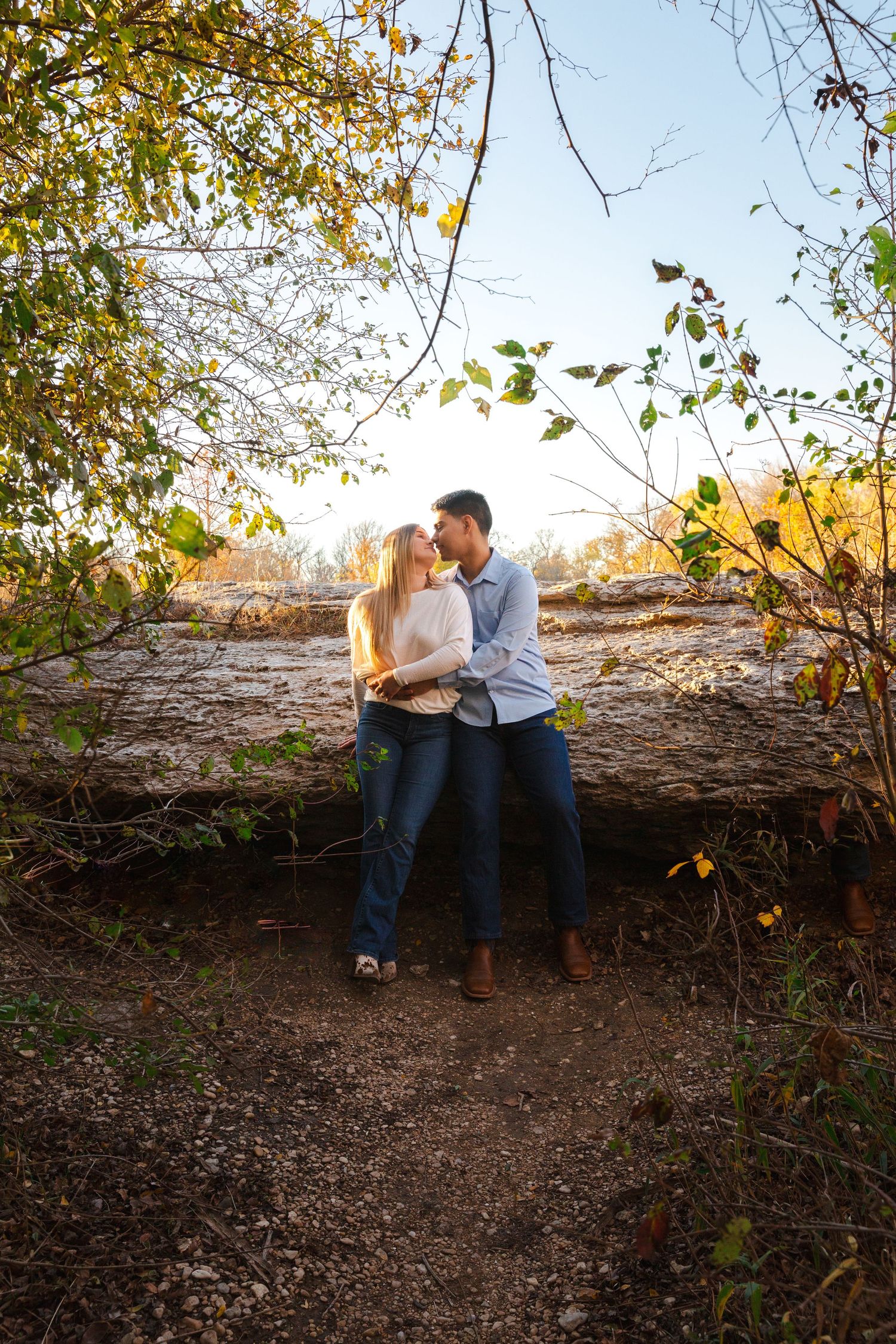 A couple embraces on a nature trail surrounded by autumn foliage.