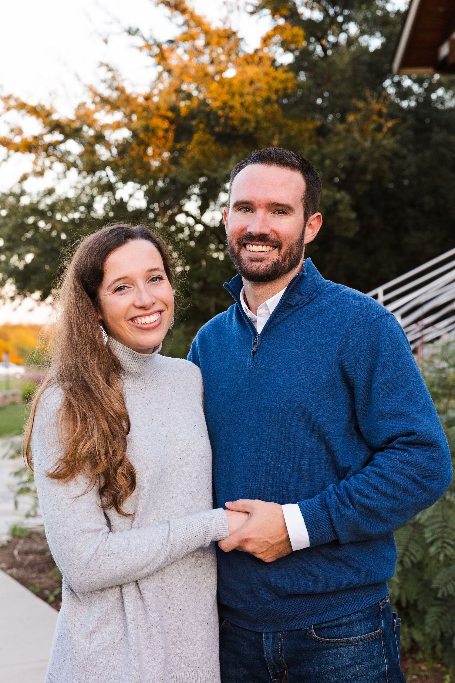 Couple in blue and grey sweaters smiles during autumn outdoor photoshoot.