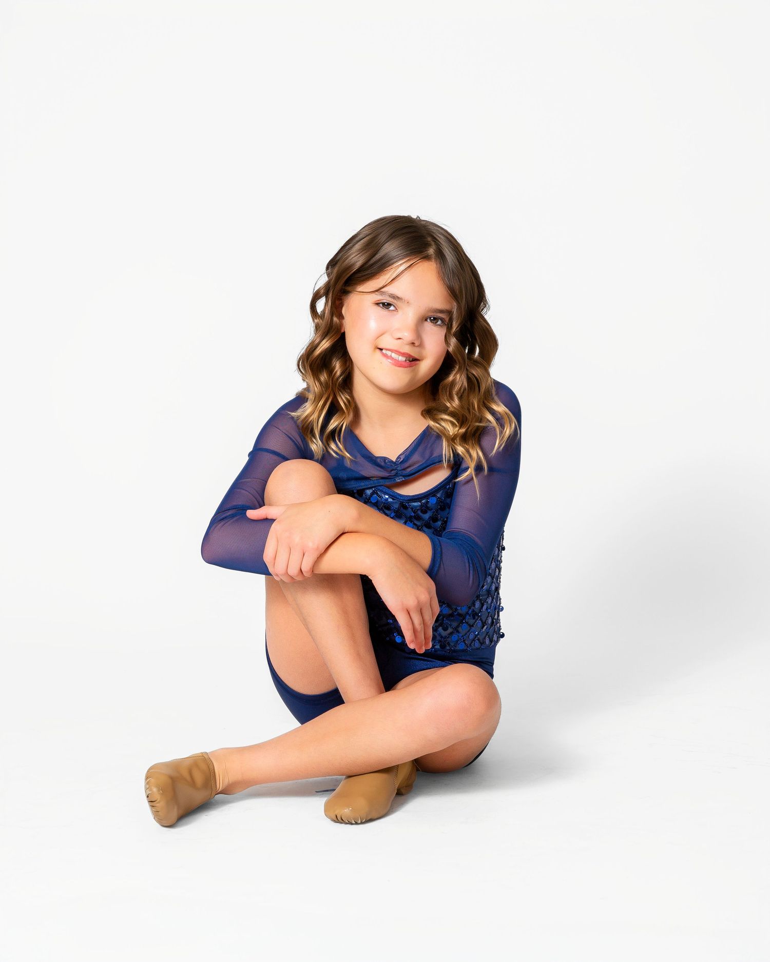 A dancer in a navy blue leotard sits posed against a white background. Dance portrait in Round Rock, TX