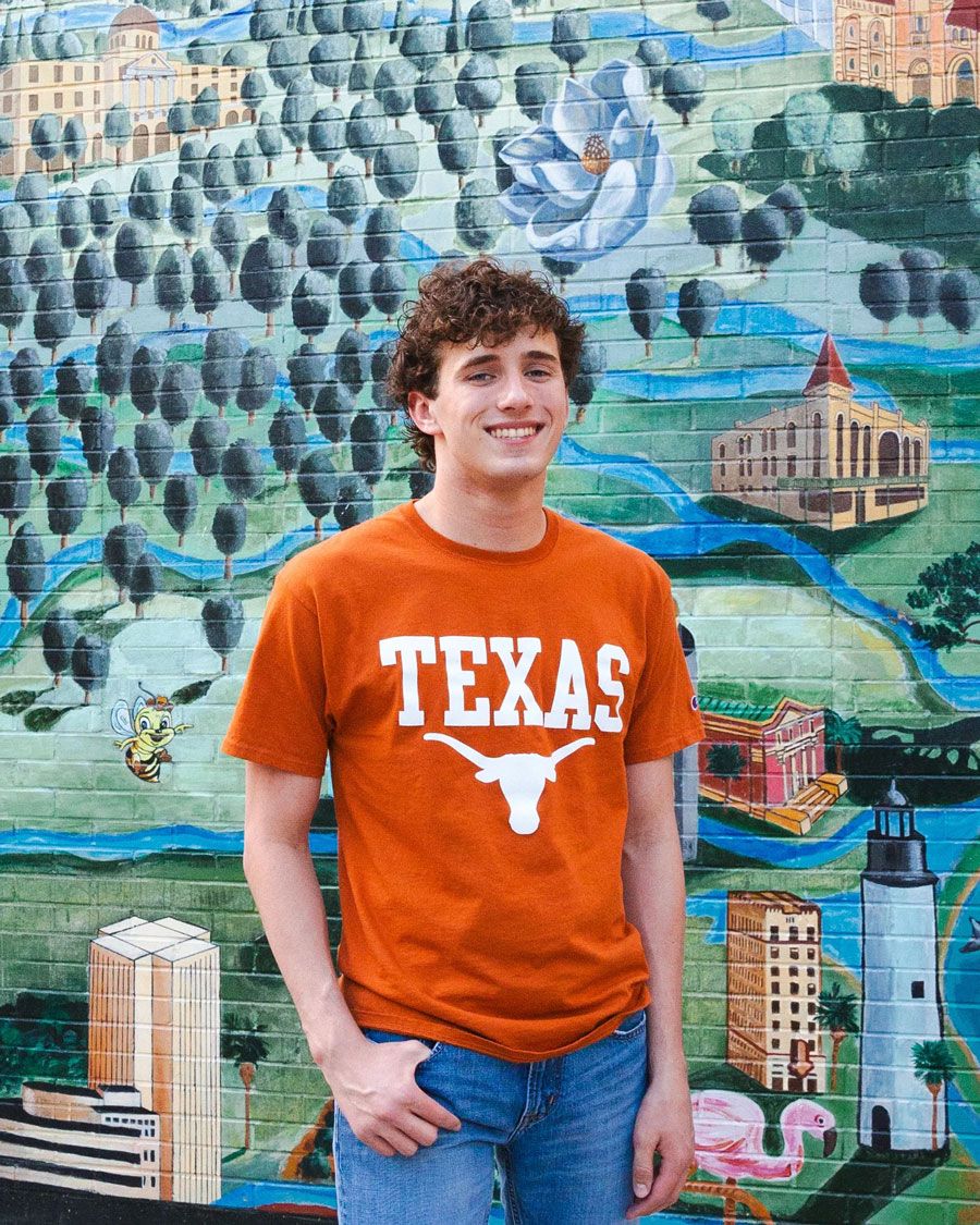 Person wearing orange Texas Longhorns t-shirt poses in front of colorful urban mural with cityscape design.