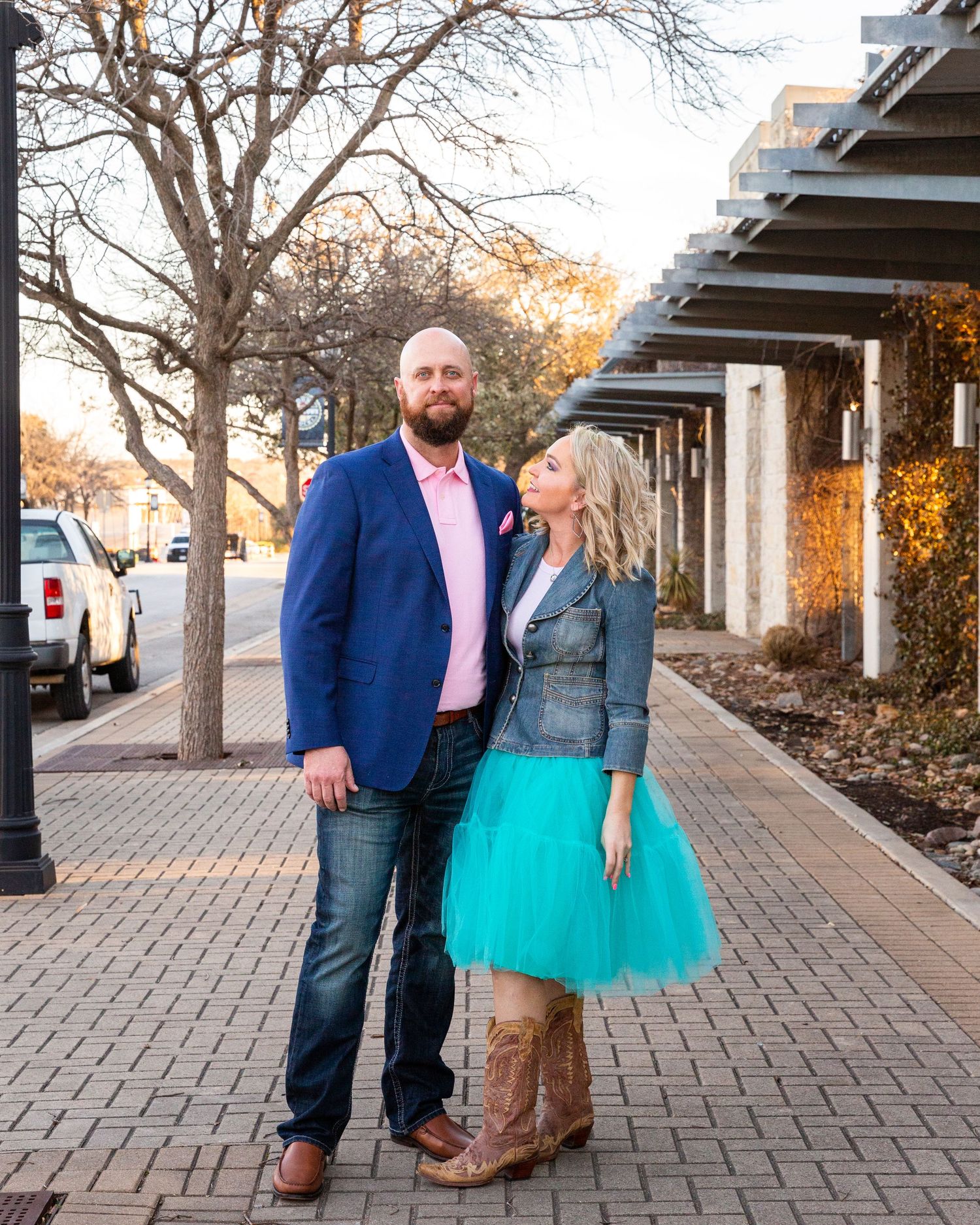 A couple poses on a brick pathway, with her wearing a teal tulle skirt and him in a navy blazer.