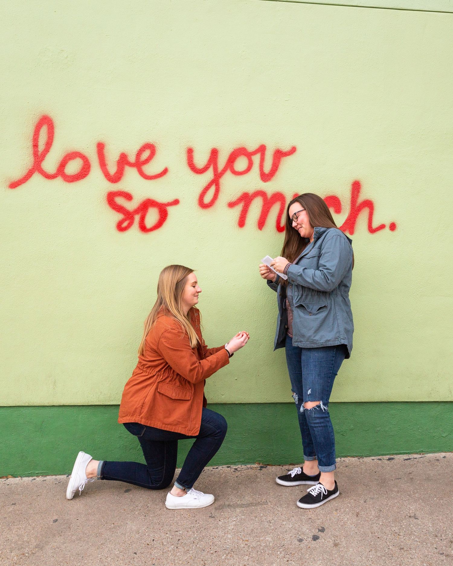 Two people sharing a sweet proposal moment in front of a green wall with red text.