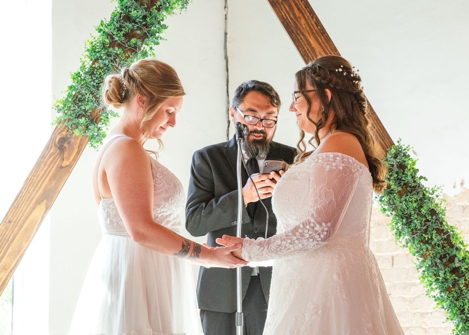 Wedding ceremony under wooden beams decorated with greenery.