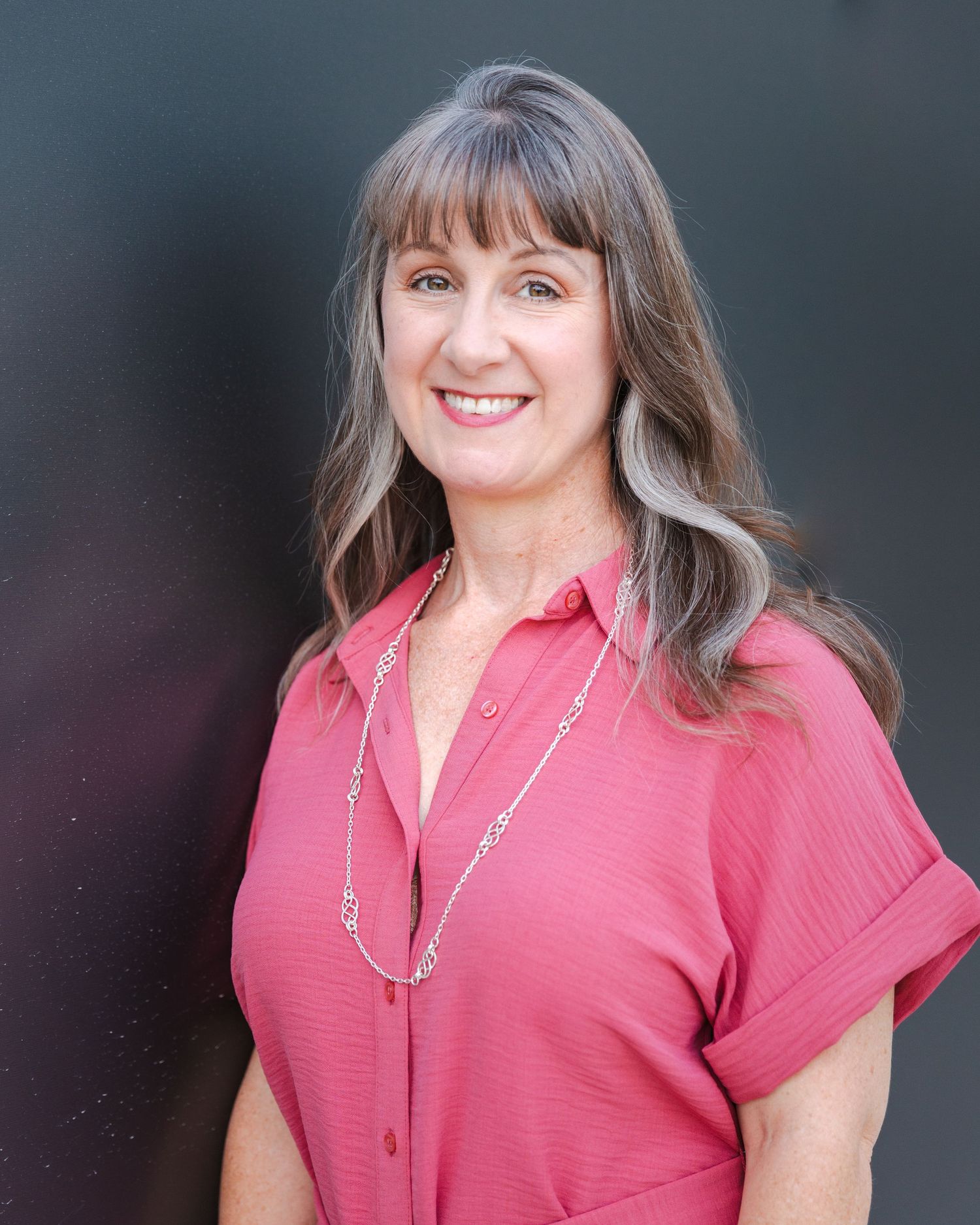 Professional headshots wearing coral pink top against dark background.