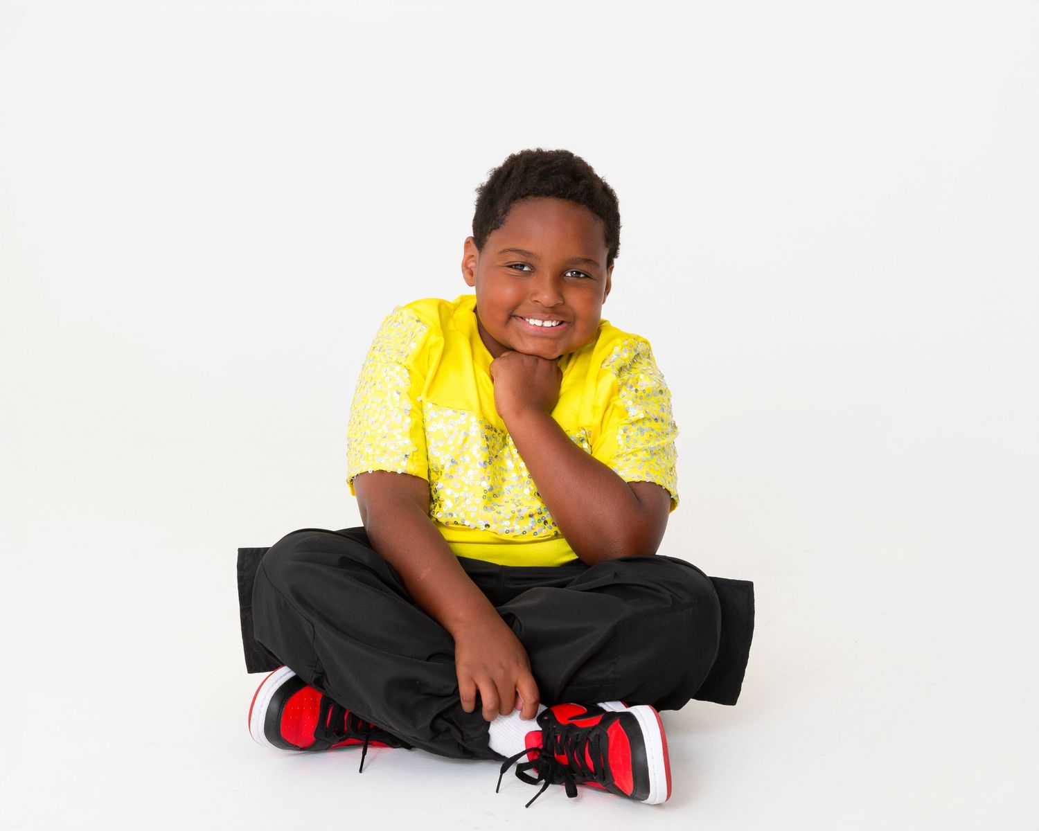 Child in bright yellow shirt and dark pants posing playfully on white background.
