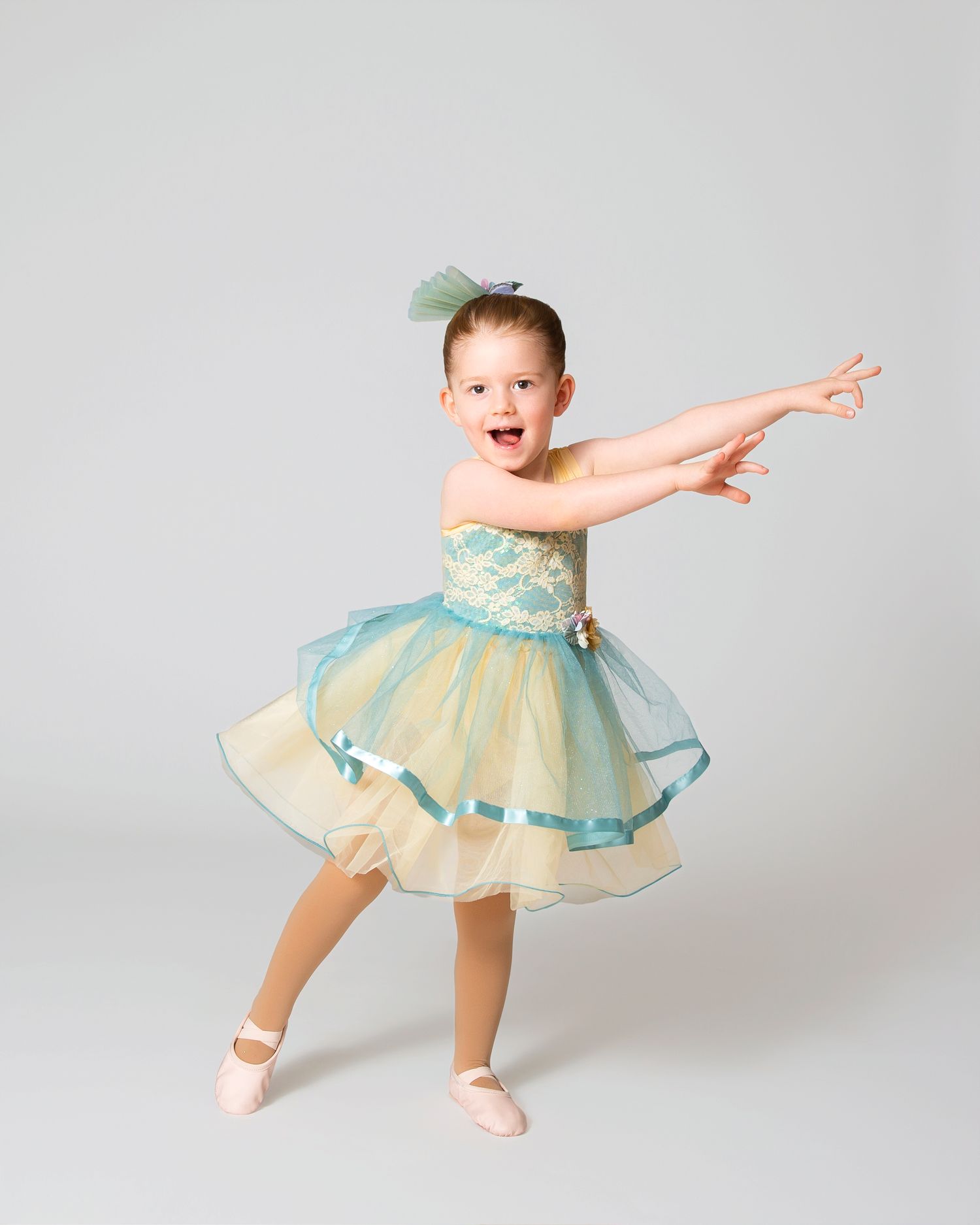 Dancer in a mint tulle dress strikes an energetic pose with arms outstretched.