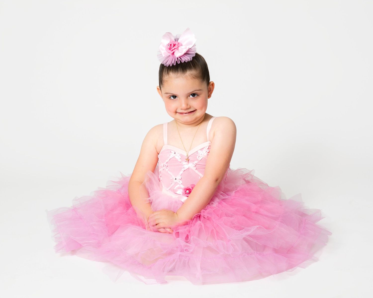 Dancer in pink tutu performs graceful ballet positions on white studio floor.