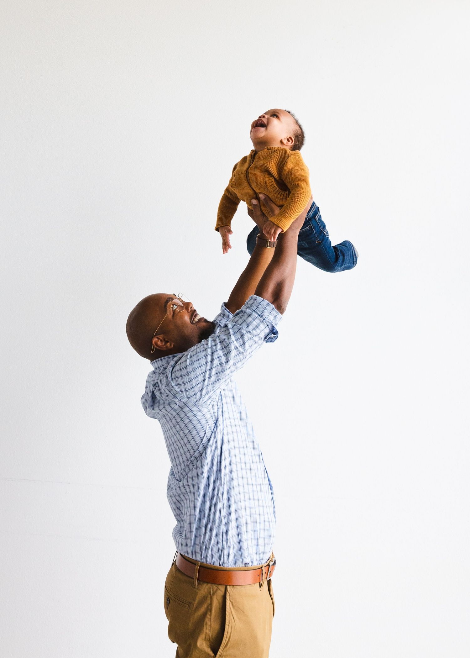 Playful moment of parent lifting child high in the air against white background. Family portrait photographer, Round Rock, TX.