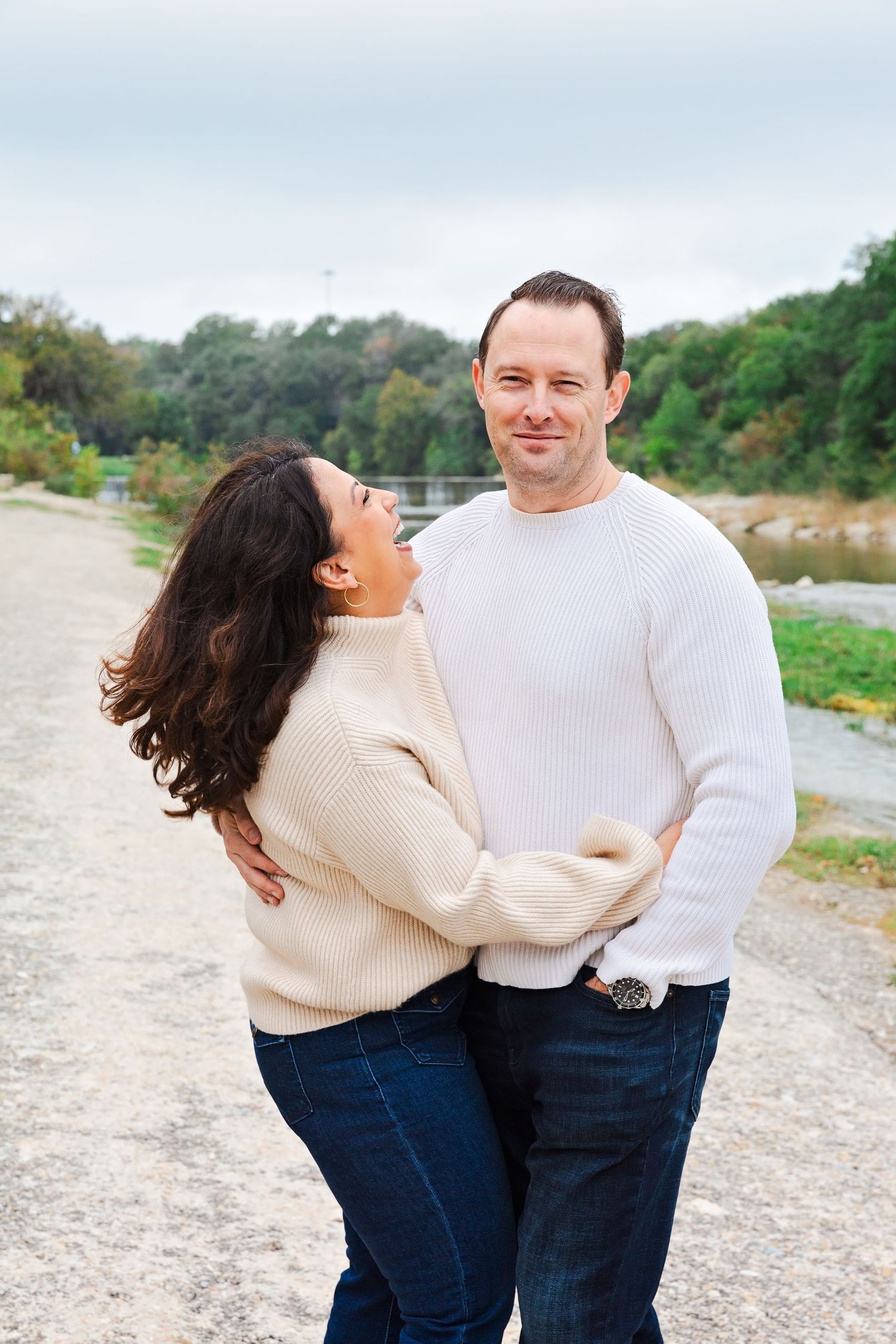 A couple in matching cream sweaters shares affectionate moments on a beach path.