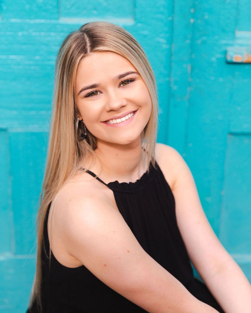 Portrait series against vibrant turquoise wall in black sleeveless top.