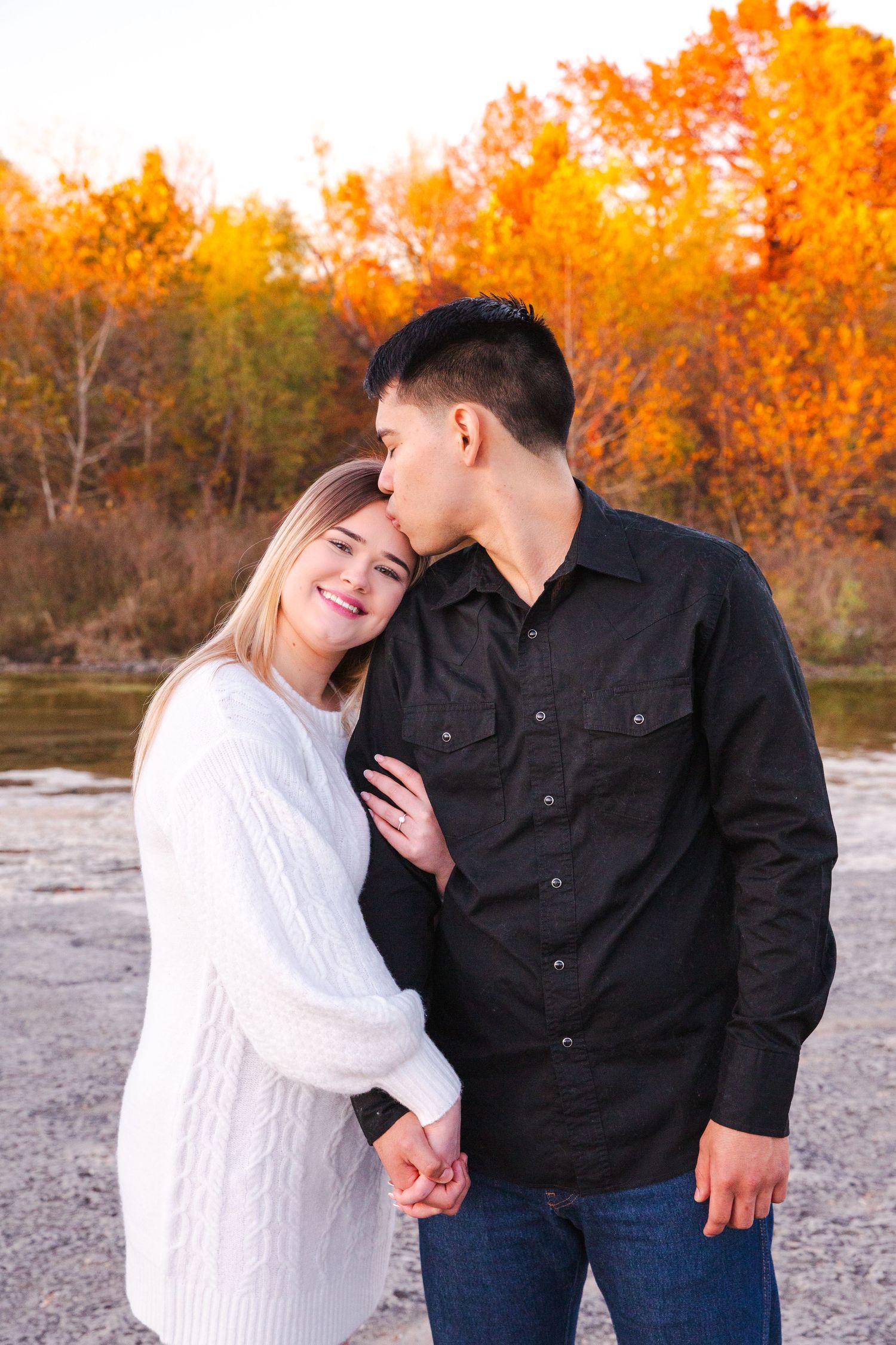 A couple shares an intimate moment against autumn foliage backdrop.