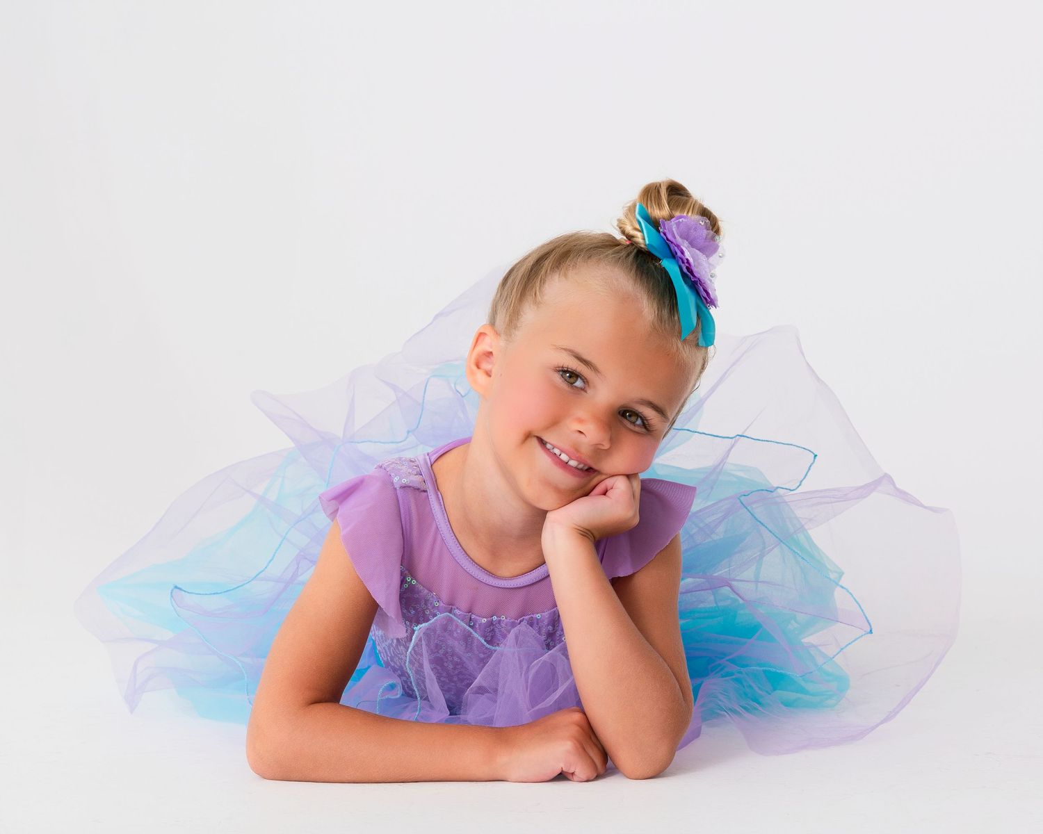 Dancer in purple and blue tulle costume poses with joyful expression.
