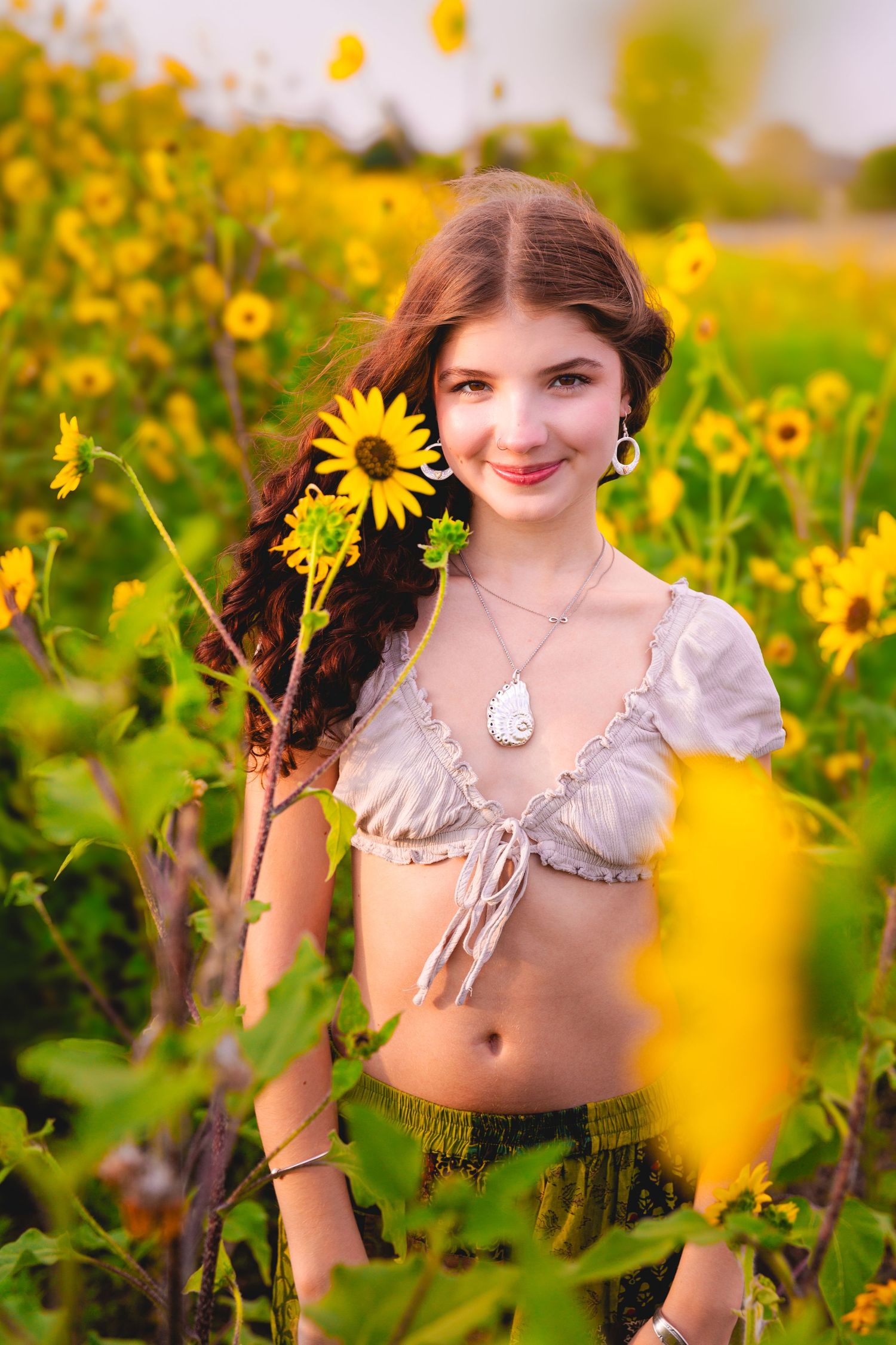 Woman in crop top poses among blooming sunflowers in summer field.