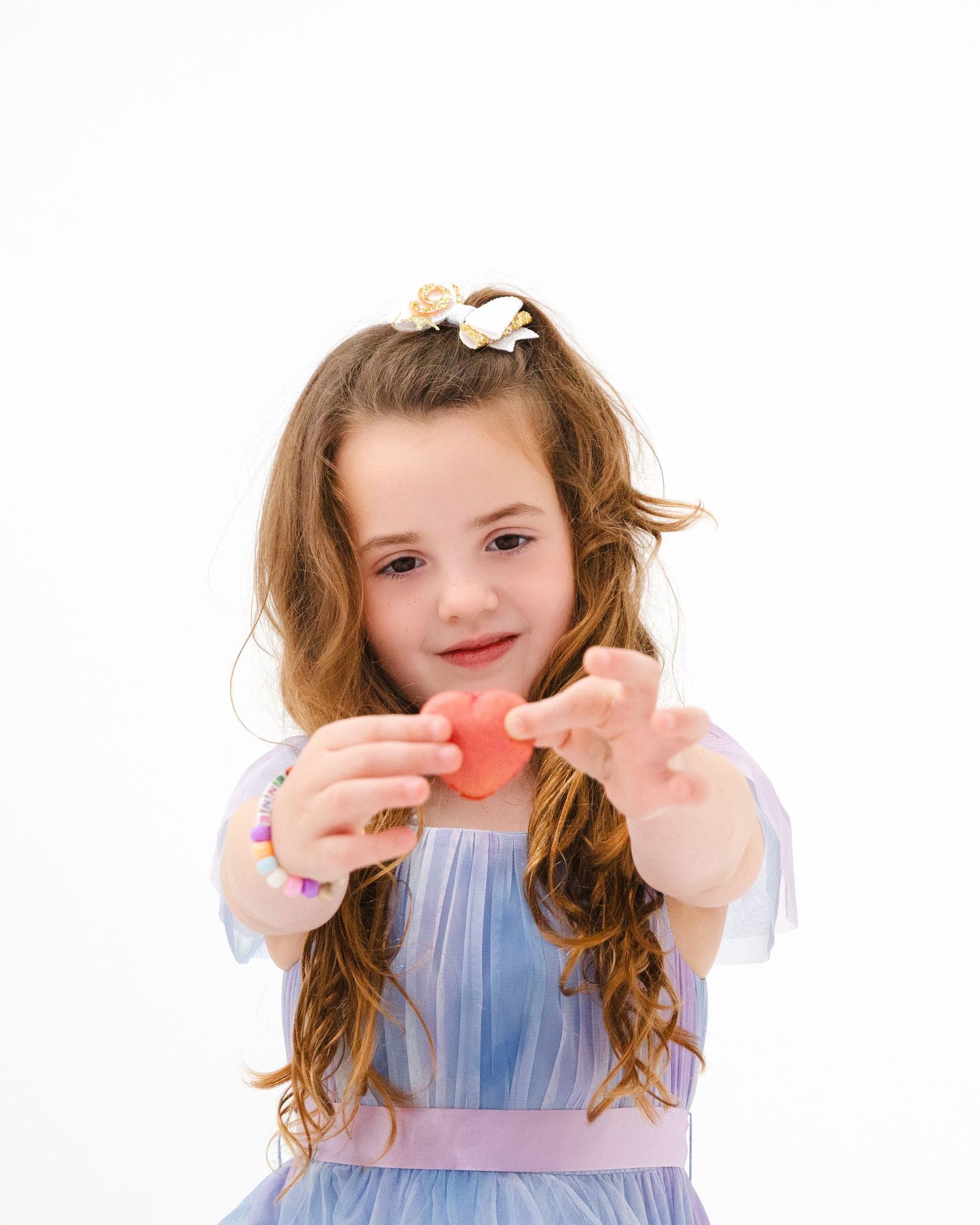 Young child in blue dress holds something small with both hands against white background.