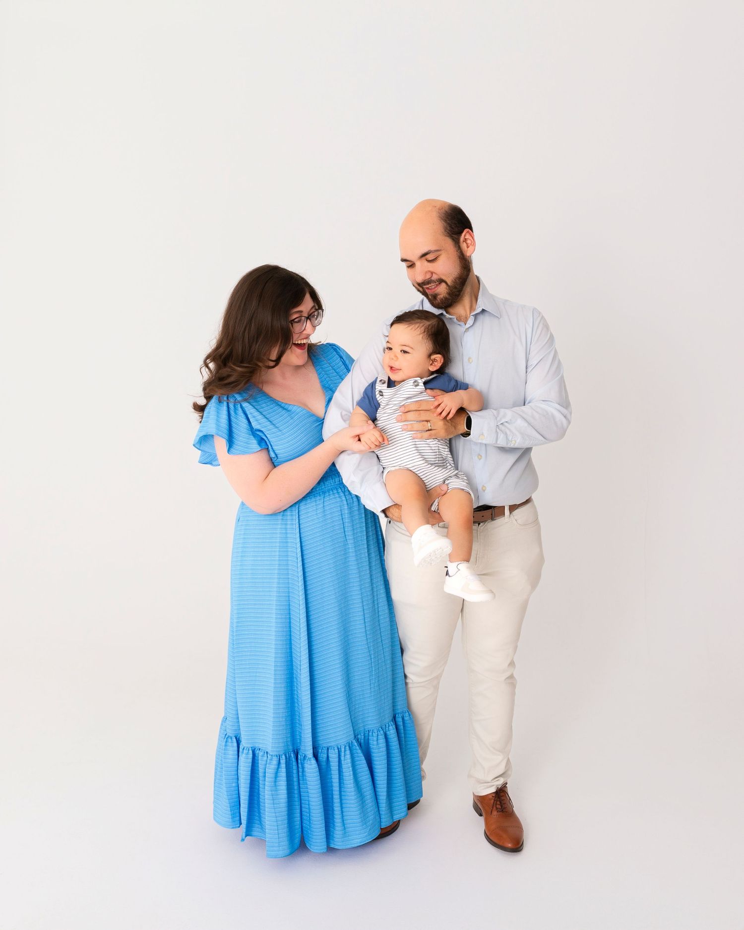 Family portrait series with parents holding and interacting with baby in light blue and white outfits.