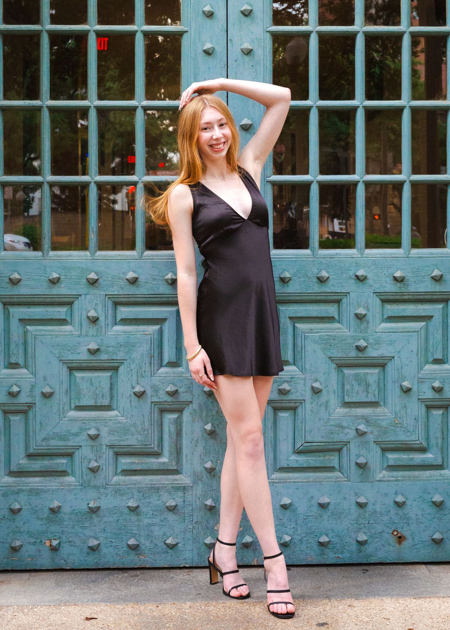 Senior portrait session on UT Austin campus. Person in black dress poses in front of ornate turquoise doors.