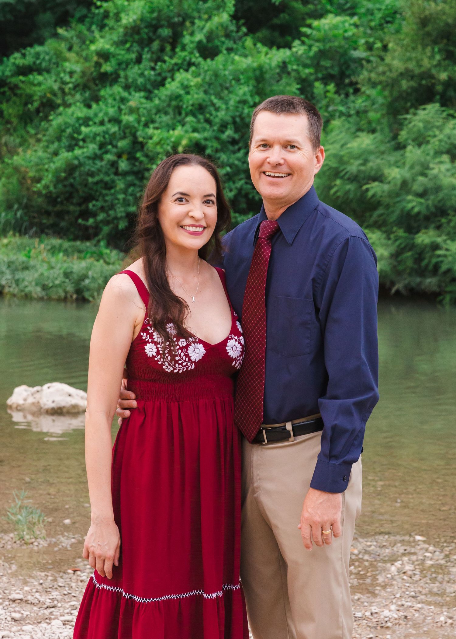 Couple in formal attire sharing romantic moments by a riverbank.