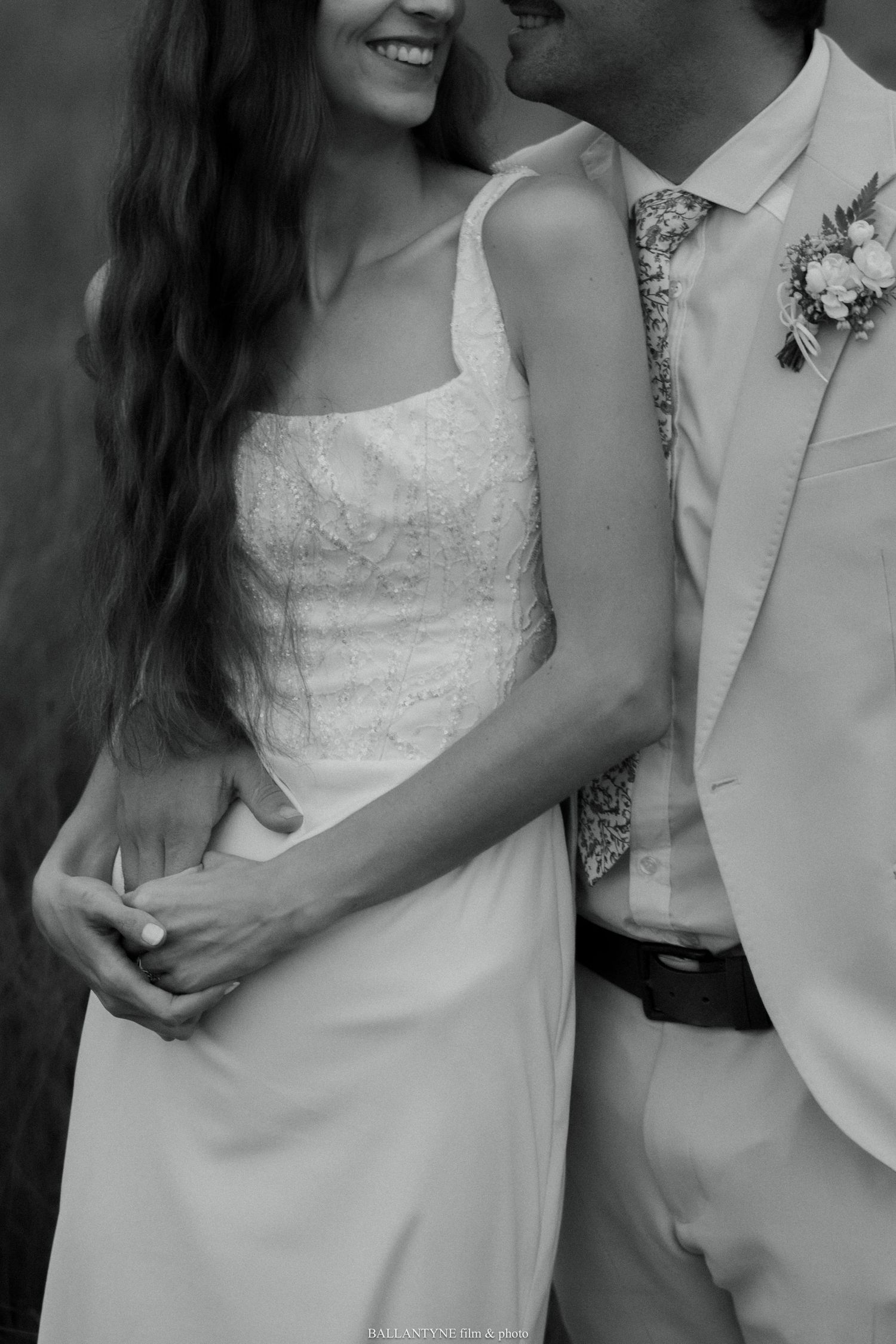 Close-up black and white photo of a bride in a lace dress and groom in a light-colored suit.
