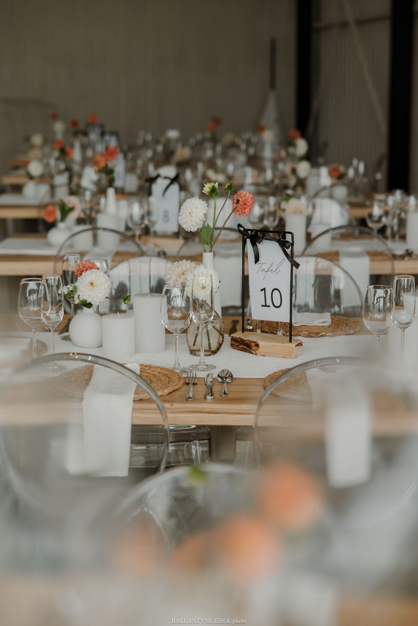 Elegant wedding reception tables with white candles, peach florals, and a table number 10 sign in a rustic venue.