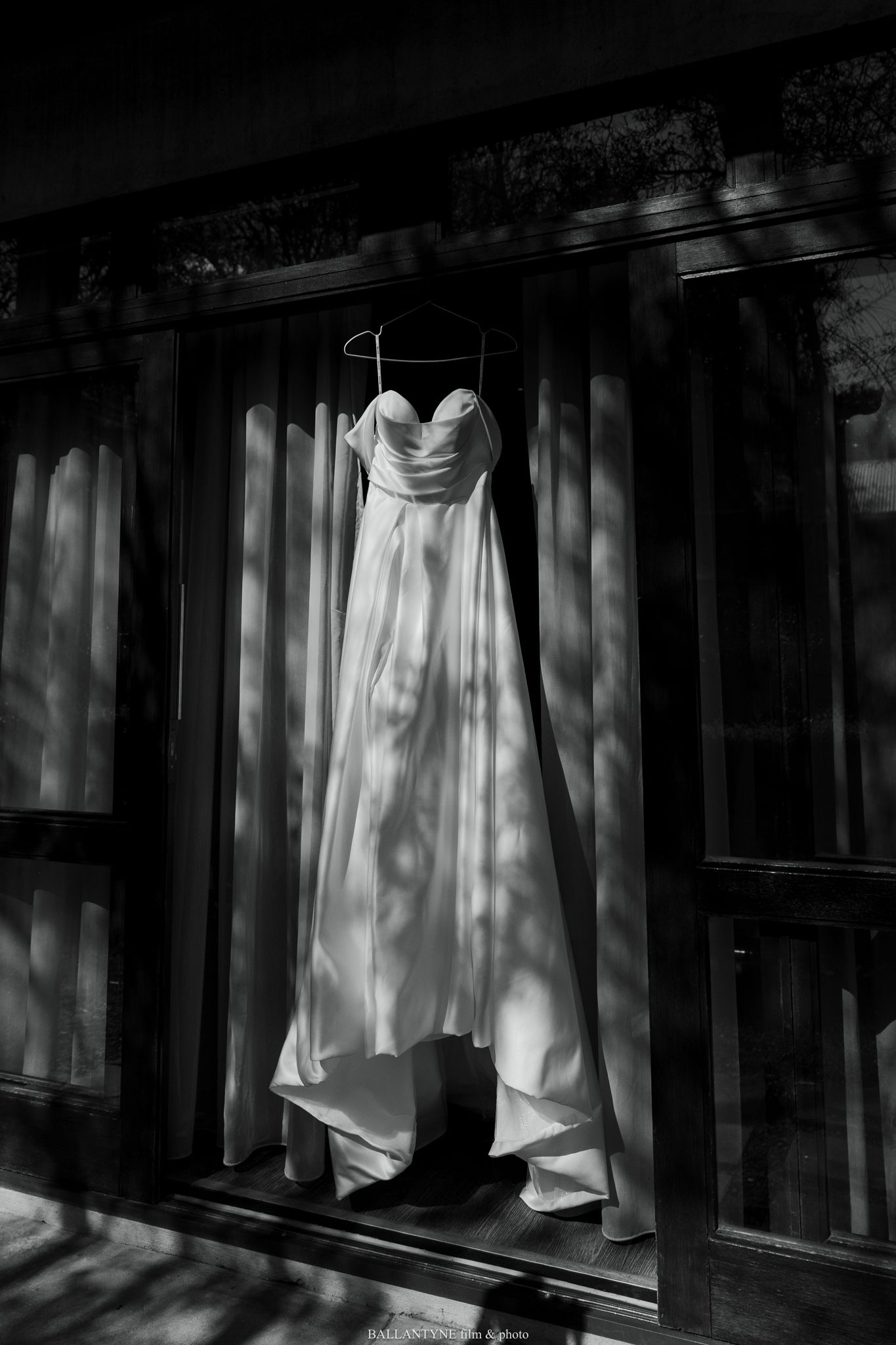 Black and white photo of wedding dress hanging in window light.