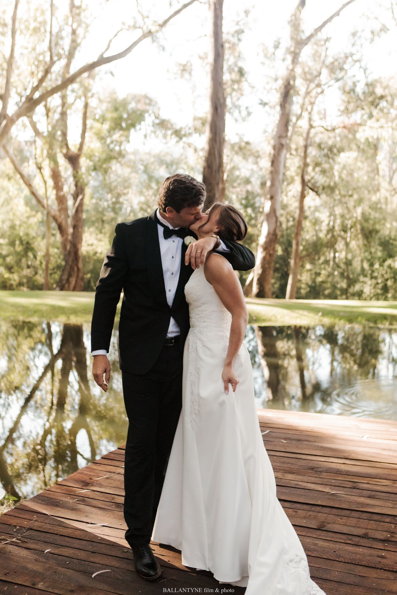Romantic wedding moment on a wooden dock overlooking a tranquil pond.