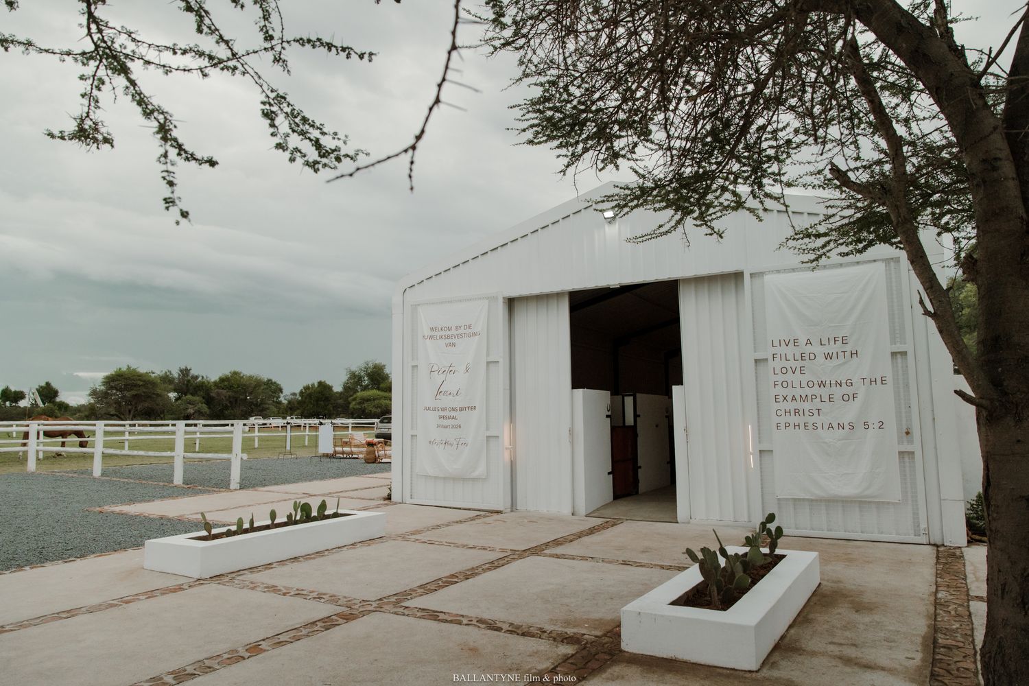 White barn venue beside a lake with engraved inspirational quotes on the walls, surrounded by manicured gardens under cloudy skies.