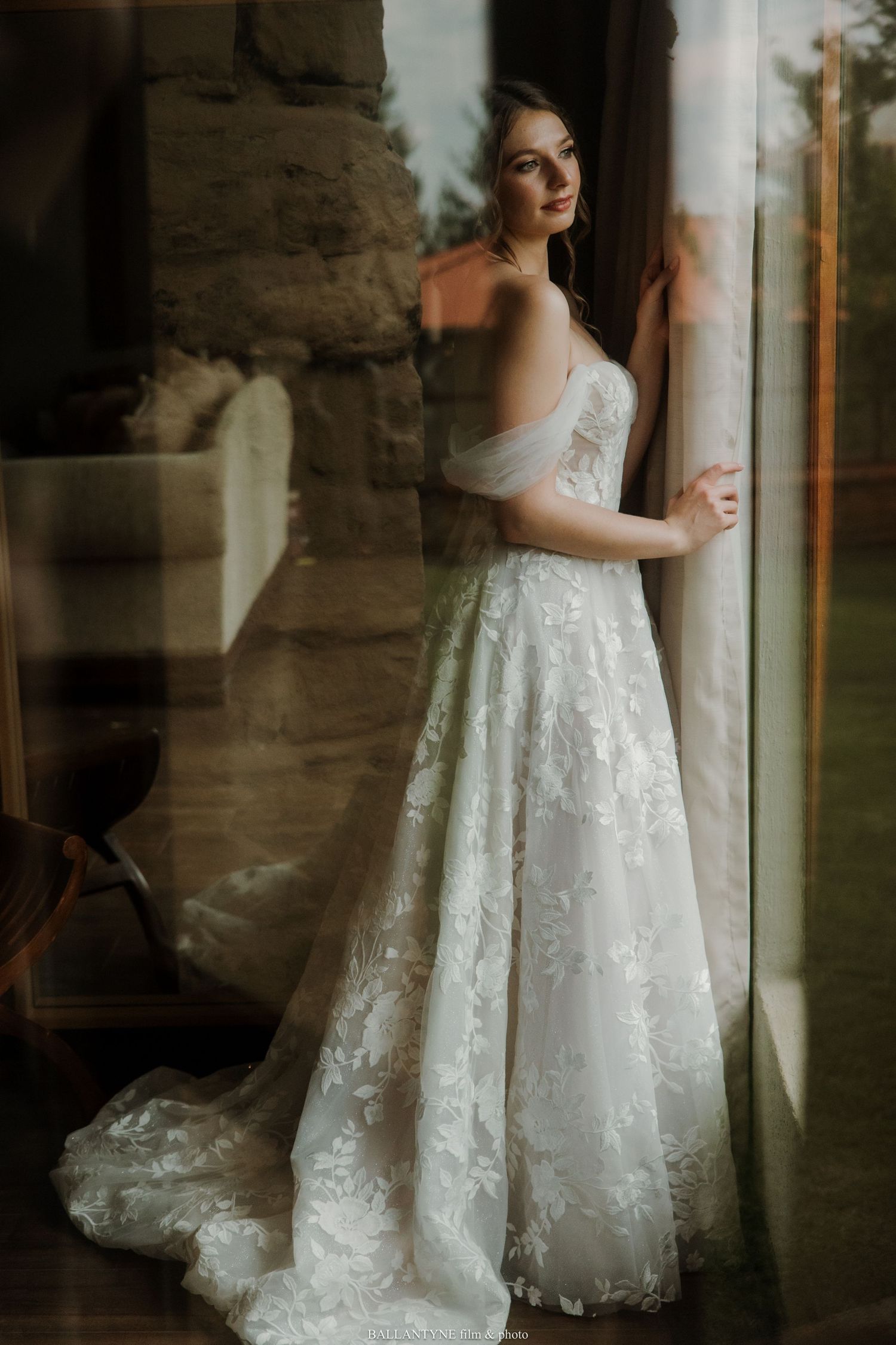A dreamy bridal portrait featuring a detailed white lace gown against stone architecture.