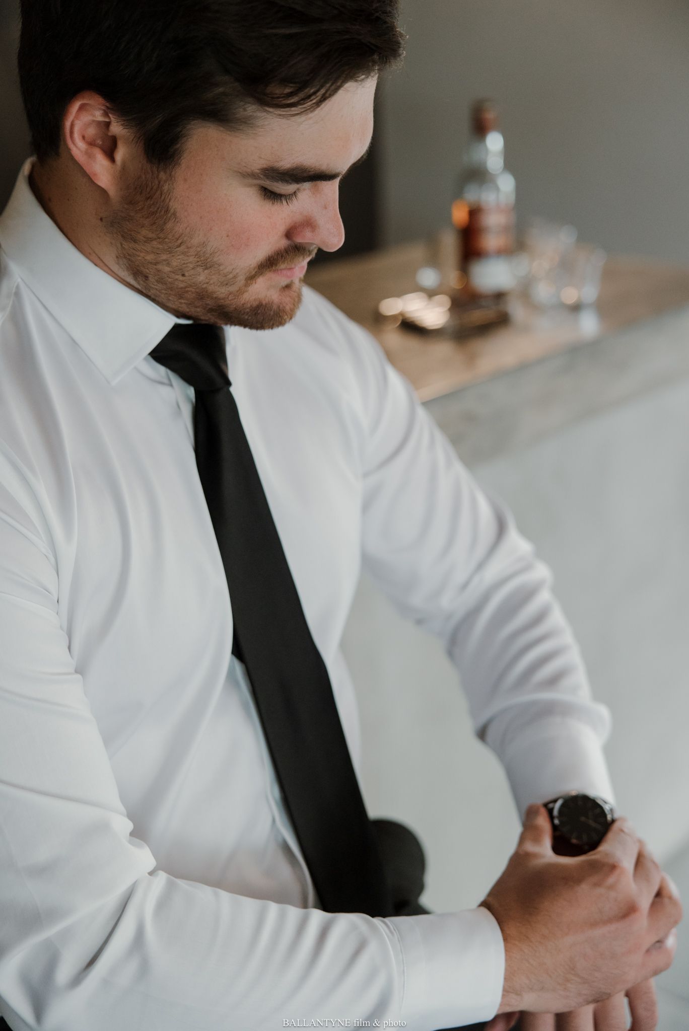 Groom in white dress shirt and black tie checking his watch before wedding ceremony.