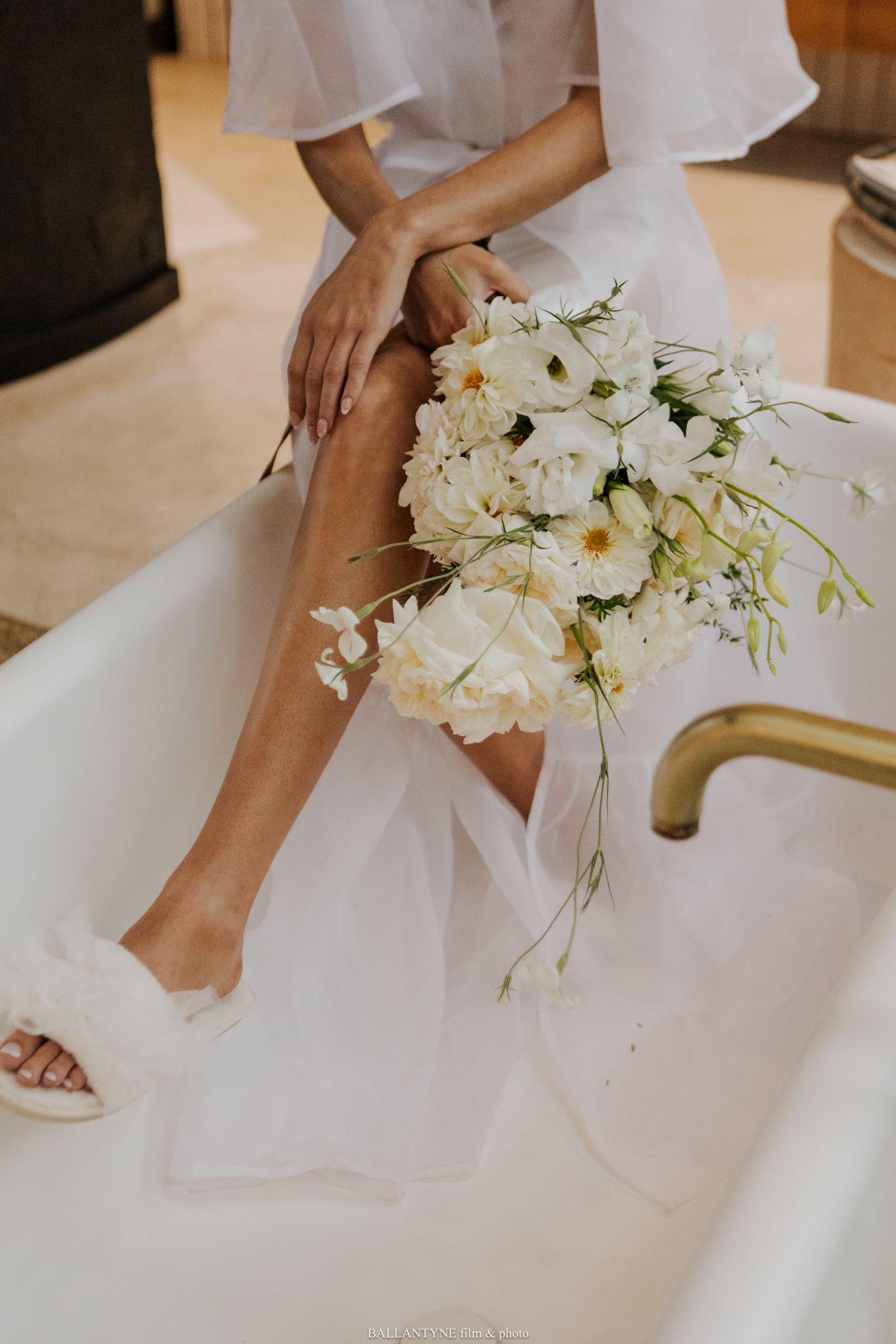 Elegant white floral bouquet next to bride's feet in white shoes.