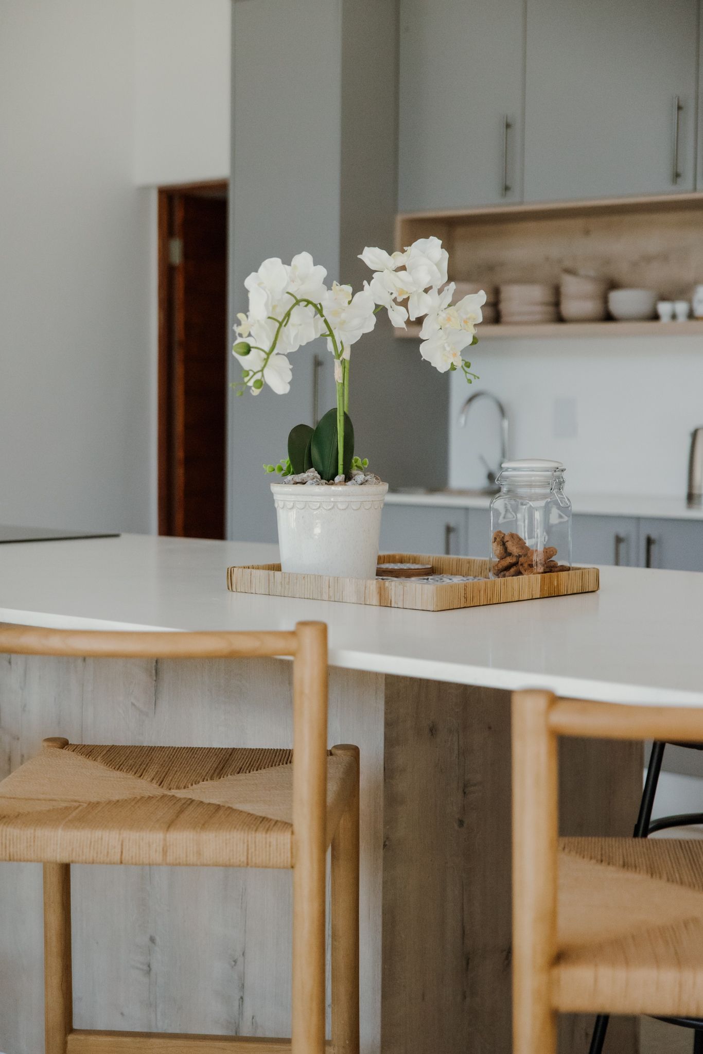 Modern kitchen counter with white marble top and wooden base featuring elegant white orchids in a ceramic vase.