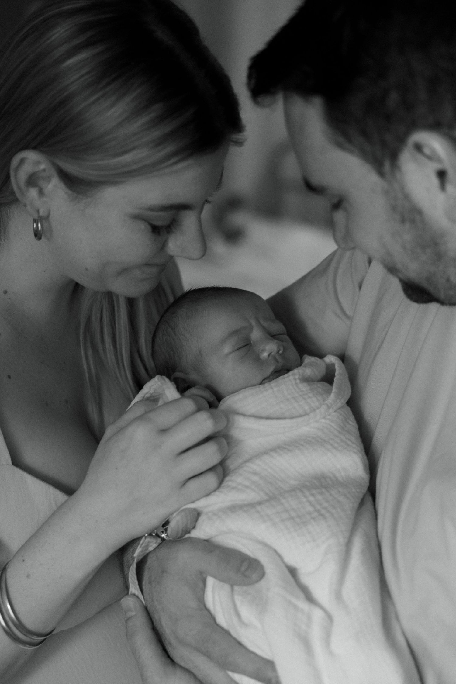 A tender black and white photo of new parents gazing lovingly at their sleeping newborn.