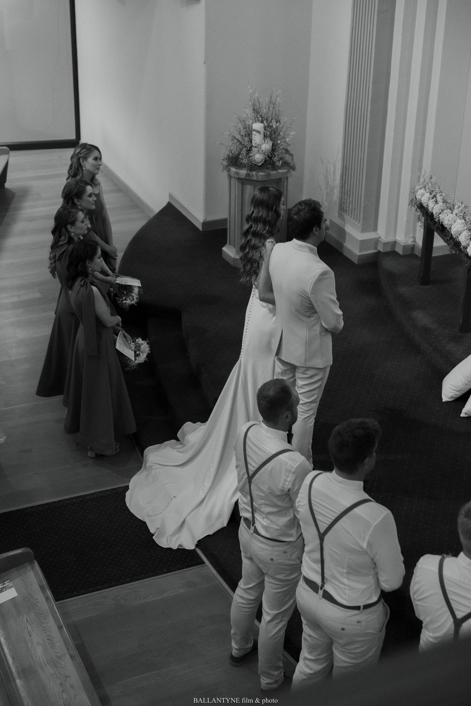 A wedding ceremony in progress showing the bridal party and groomsmen in formal attire standing at the altar.
