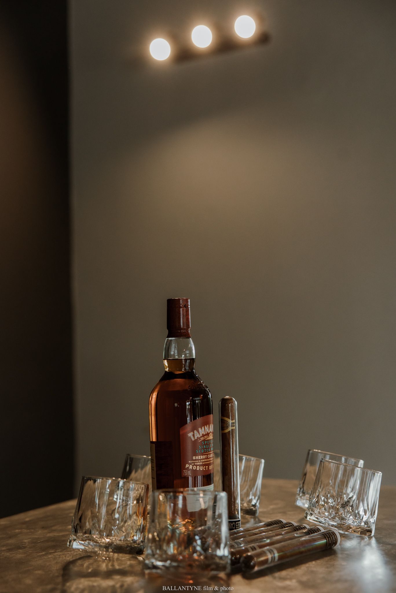 Tannr whisky bottle surrounded by crystal glasses and cigars on a marble table with warm ambient lighting.