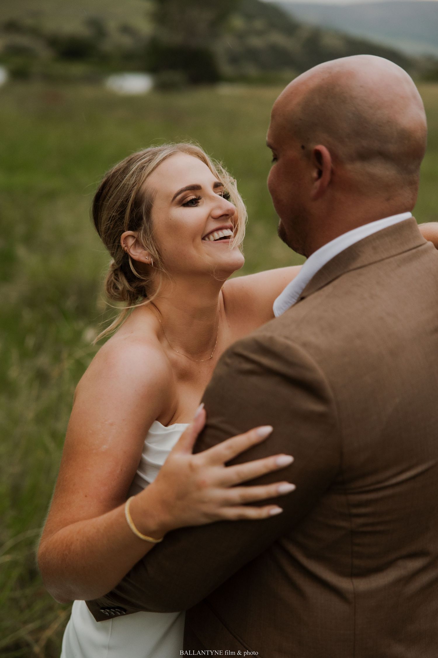 A joyful wedding moment captured outdoors as a couple shares a laugh against a natural landscape.