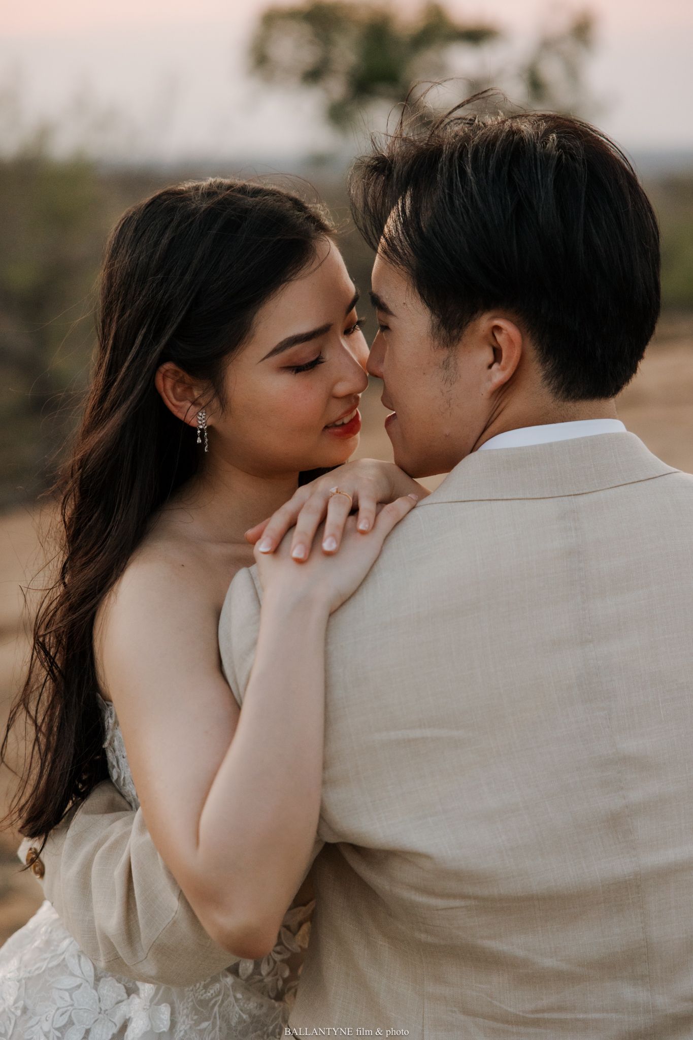 Romantic couple in white and beige attire share intimate moments during a sunset photoshoot.
