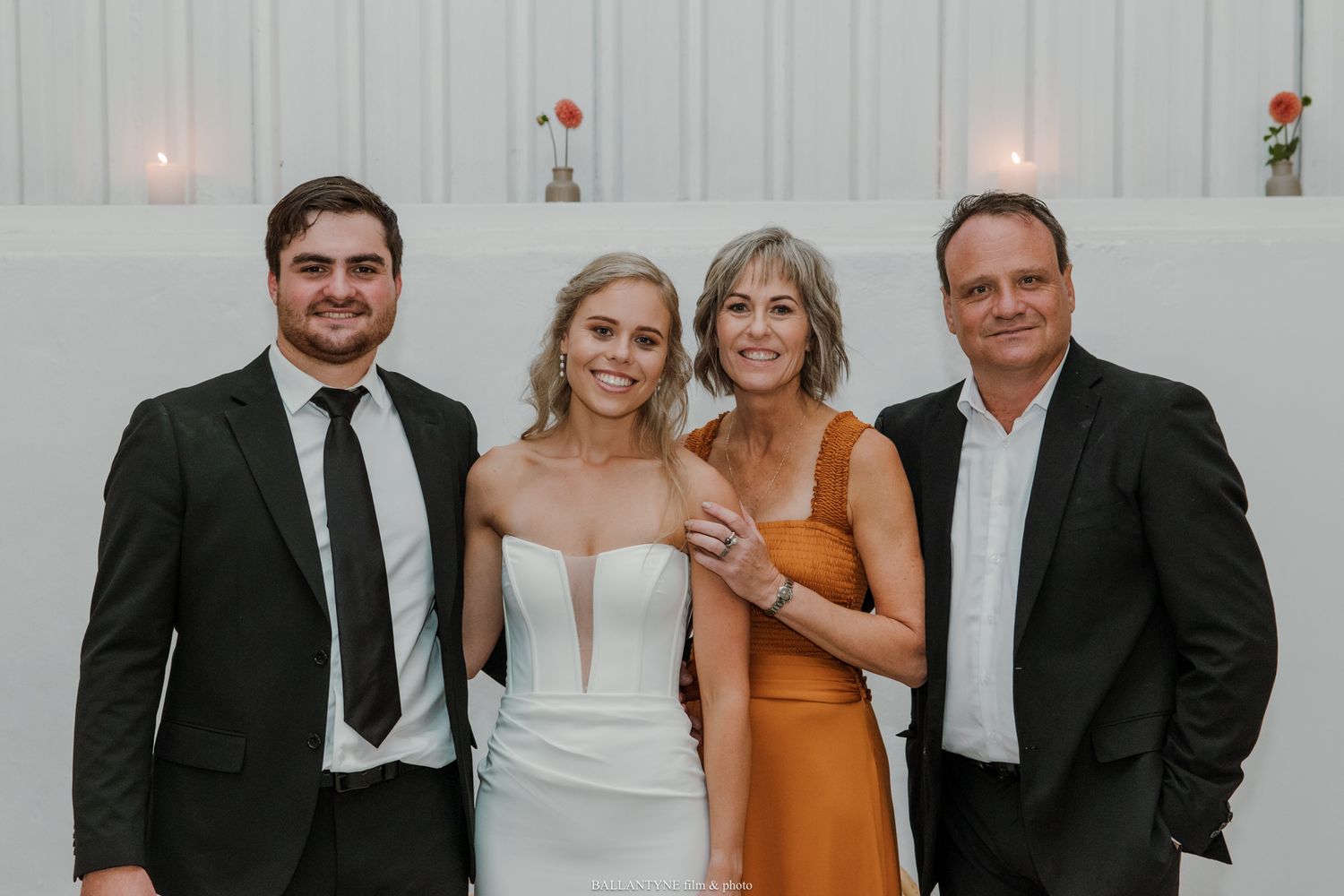 Family of four posing together at a wedding reception, dressed in formal attire, smiling at the camera.