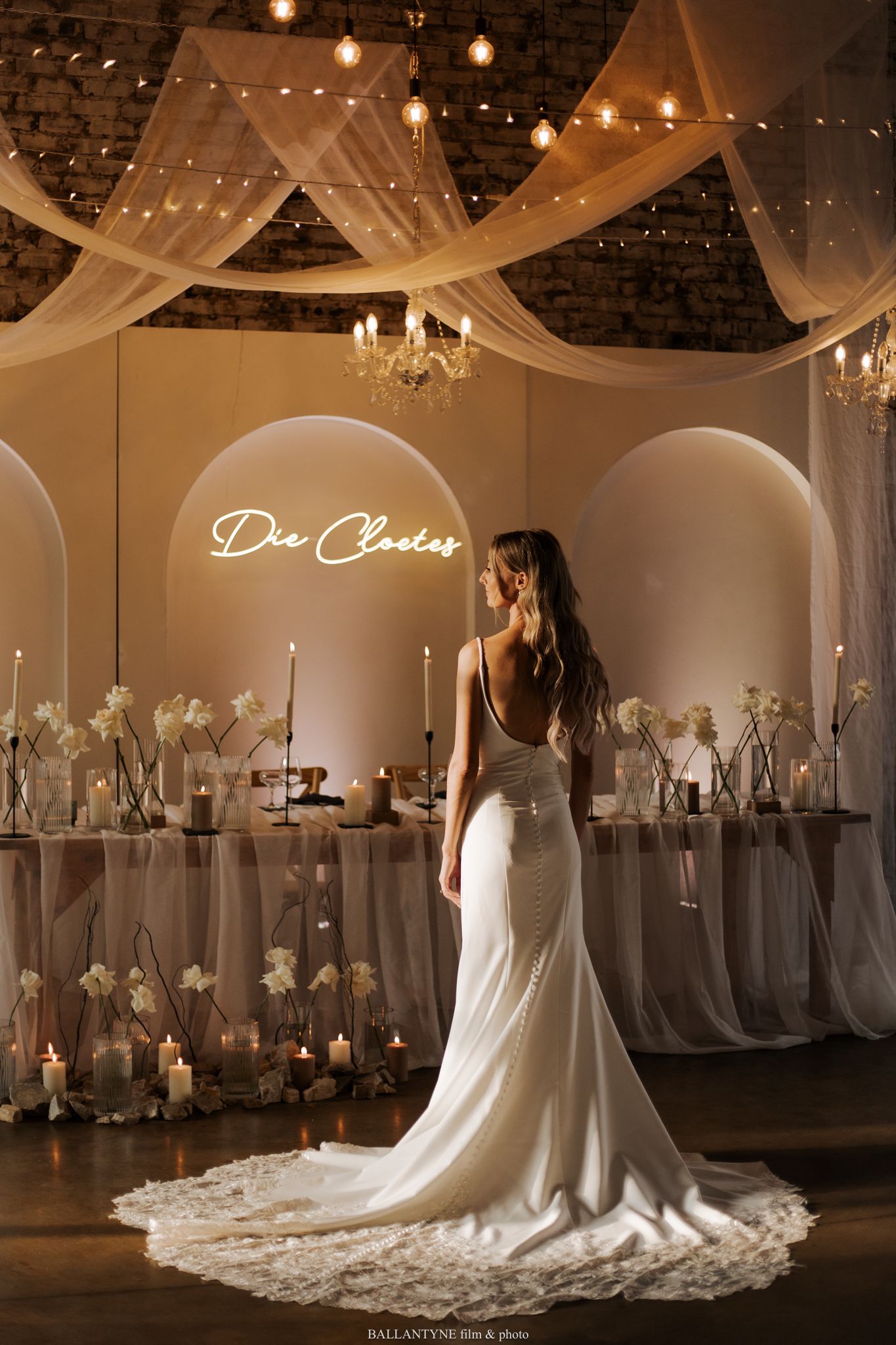 A bride poses in an elegant white gown under romantic lighting and draped decor.