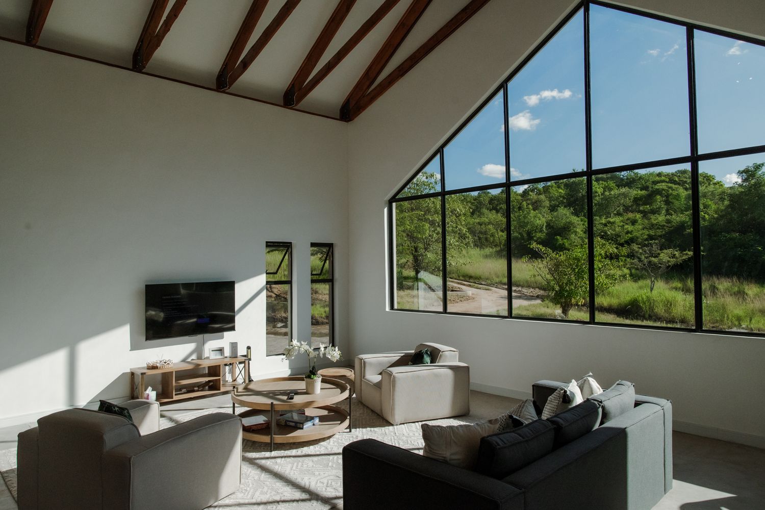 Modern living room with large angular windows, natural light, and contemporary furniture in a minimalist setting.