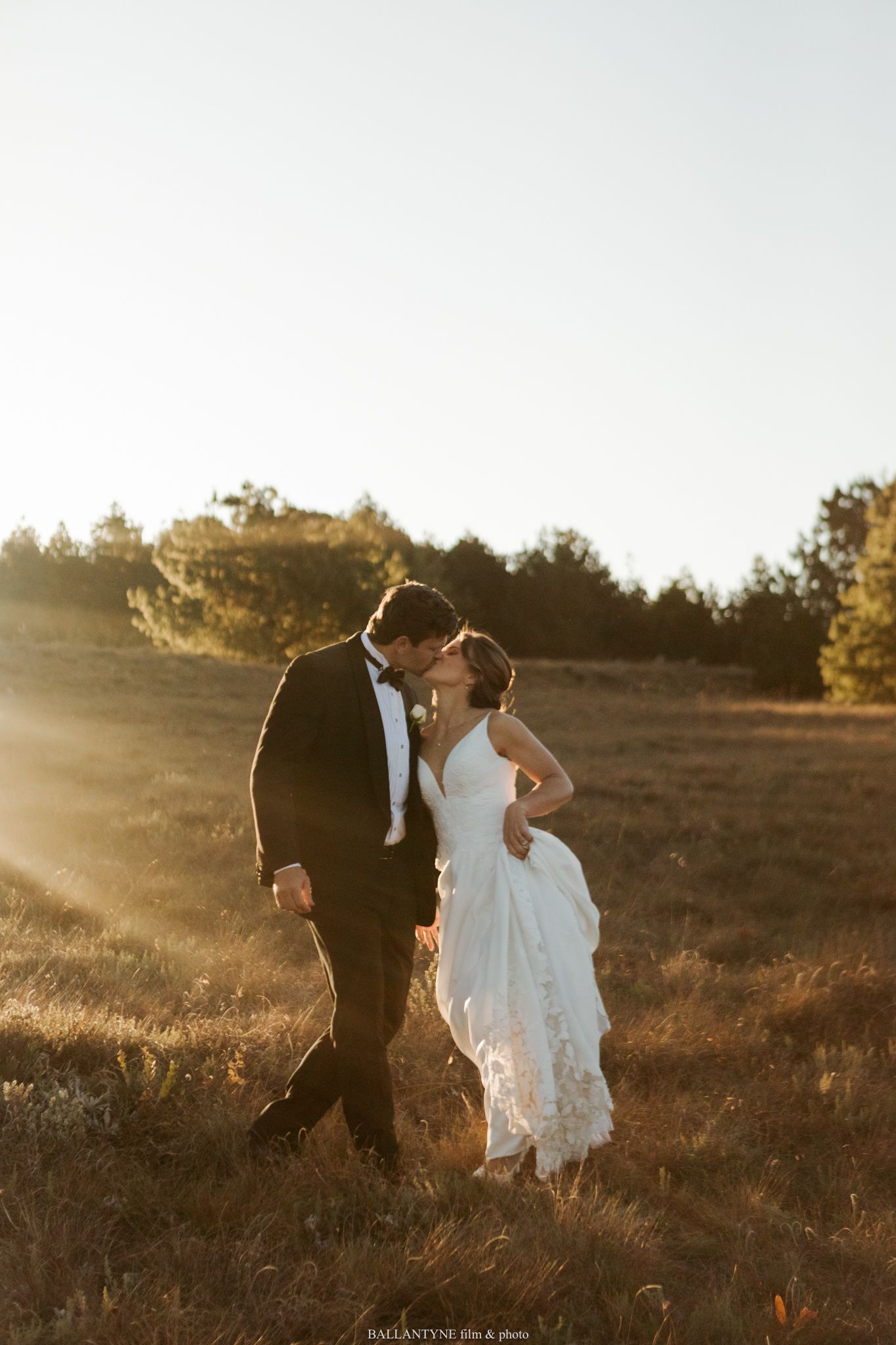 Newlyweds walking through a sunlit field at golden hour.