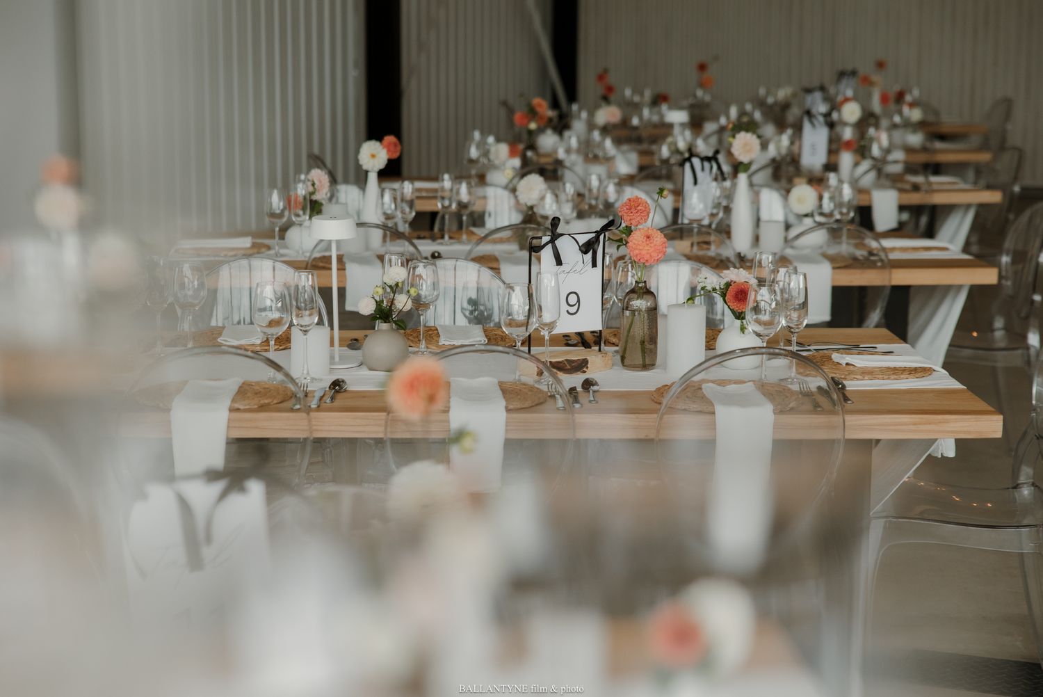 Elegant wedding reception tables with blush floral centerpieces, candles, and table numbers in a bright venue.