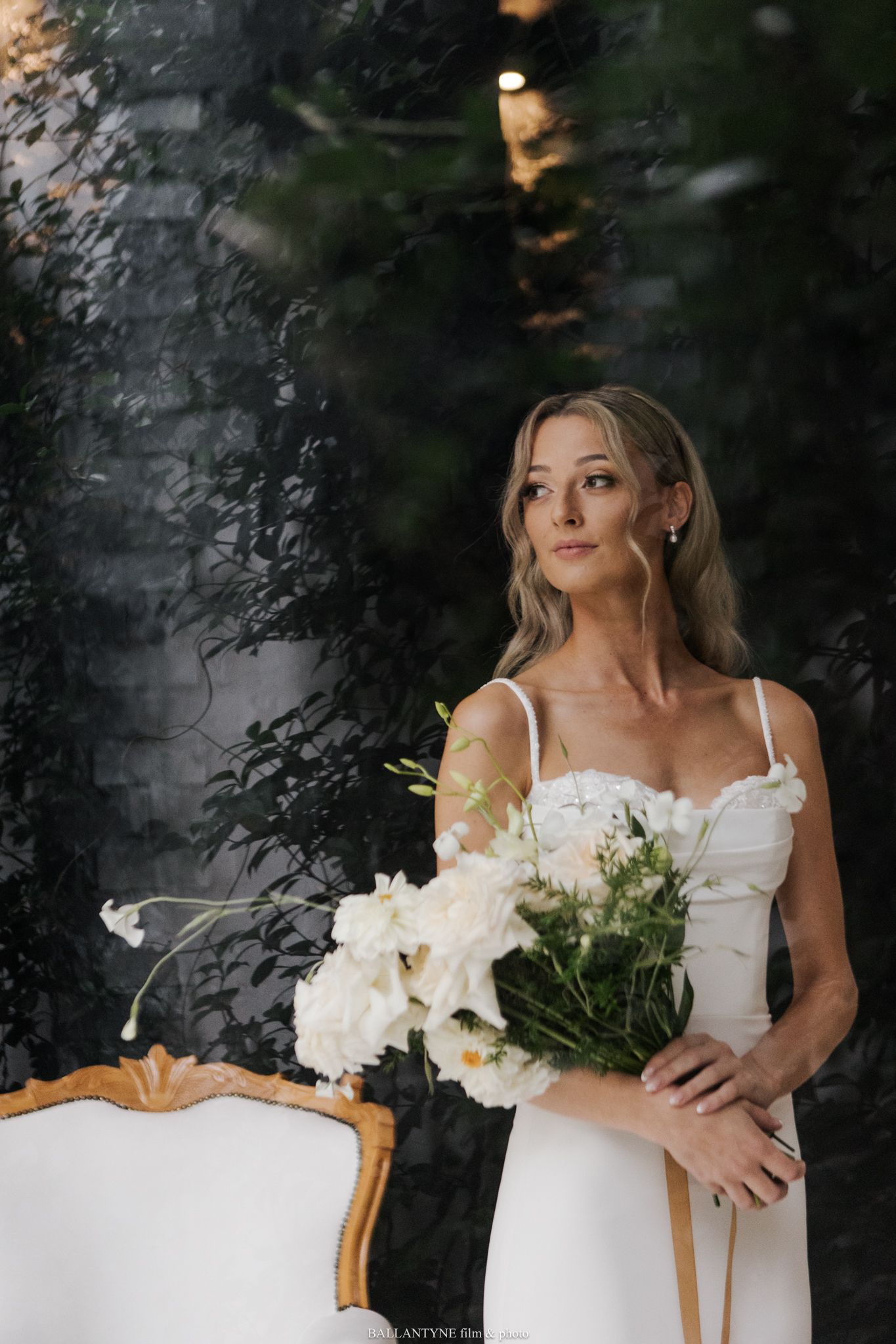 A bride holds a bouquet of white flowers against a dark dramatic background.
