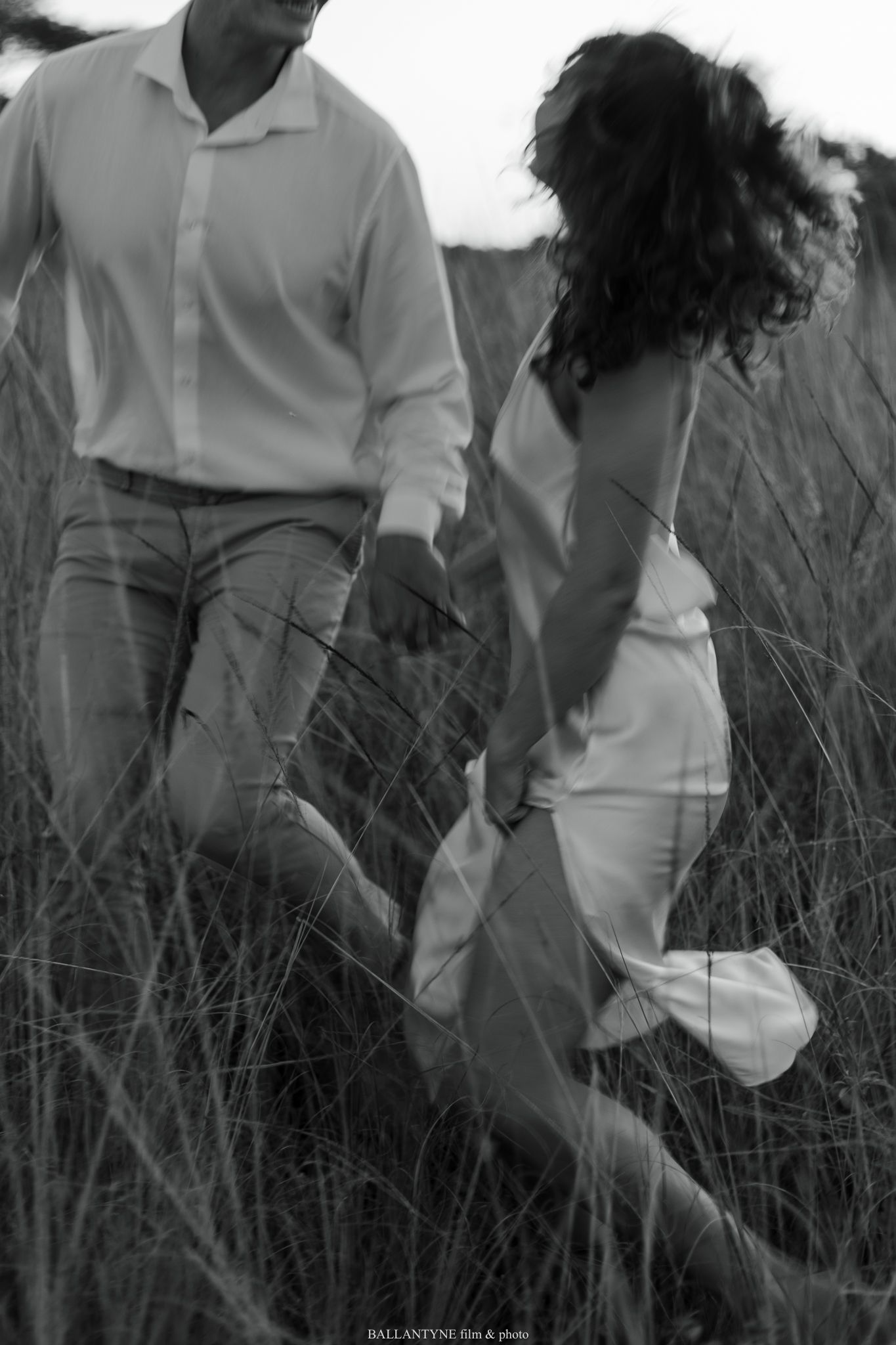 Black and white photo of couple walking through tall grass field. Engagement, engaged couples.