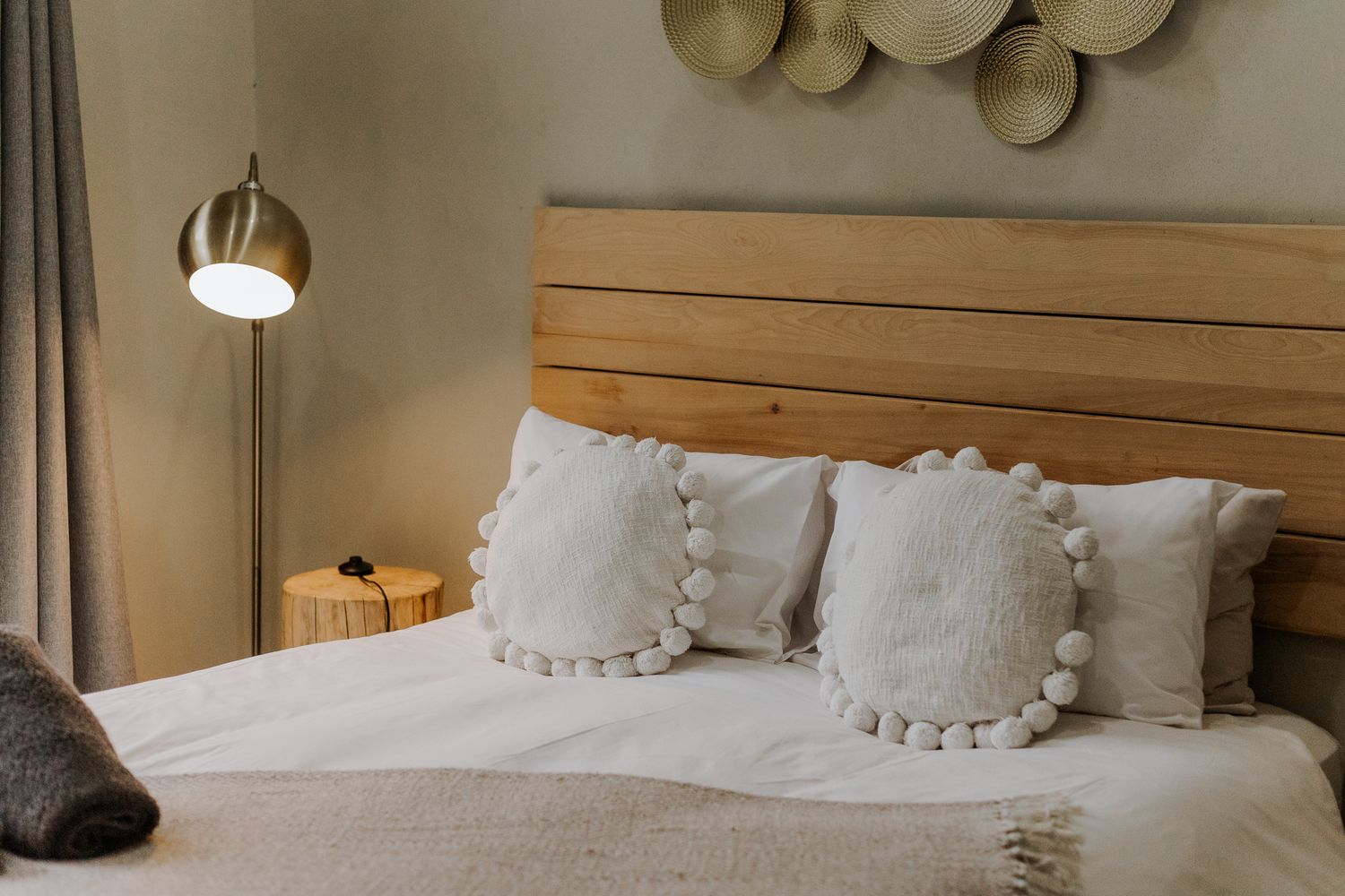 A cozy bed with white linens and multiple plush pillows arranged against a wooden headboard in a rustic bedroom.