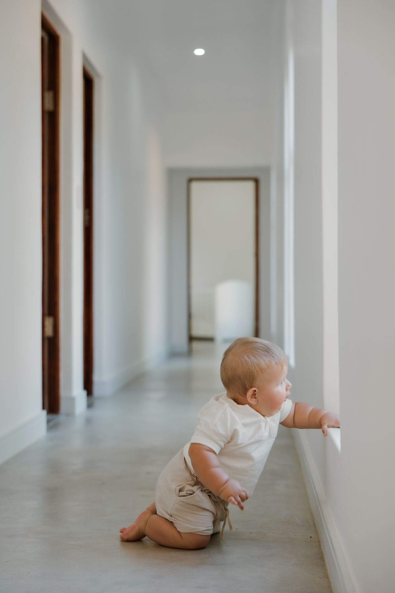 A sequence of photos showing a baby in white onesie crawling along a bright hallway with wooden door frames.