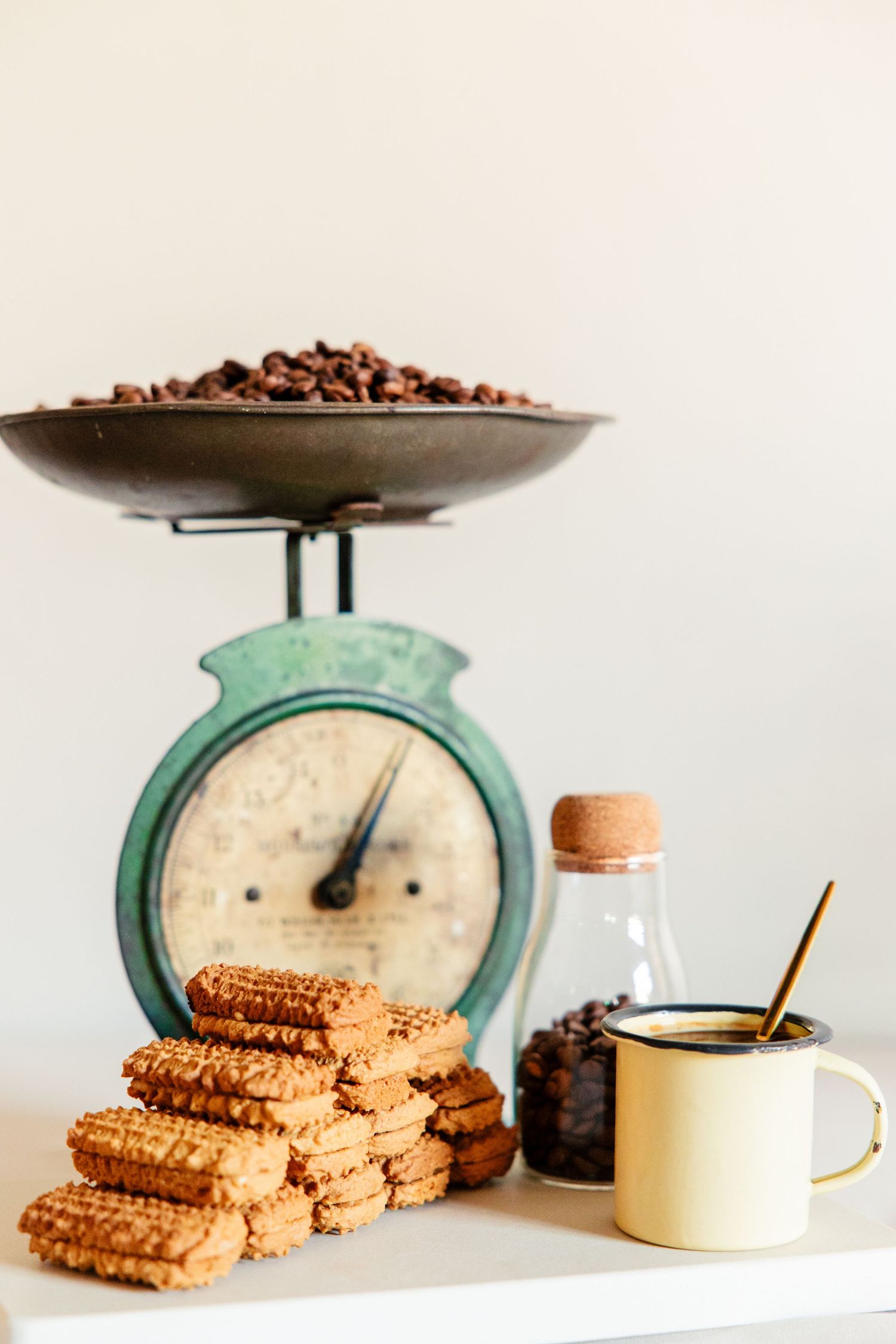 Vintage mint green kitchen scale with coffee beans and stacked brown cookies arranged in a minimalist composition.