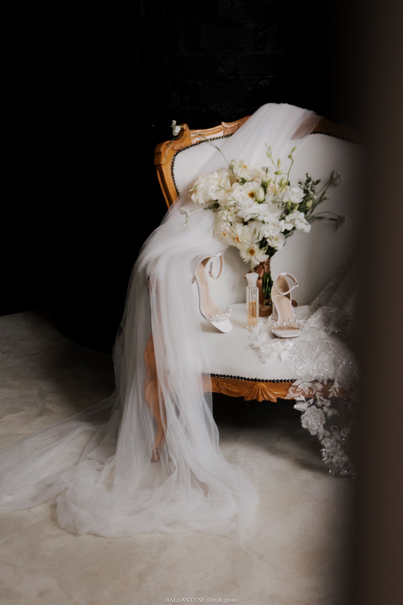 Wedding dress with flowing veil arranged on vintage chair with floral accents.